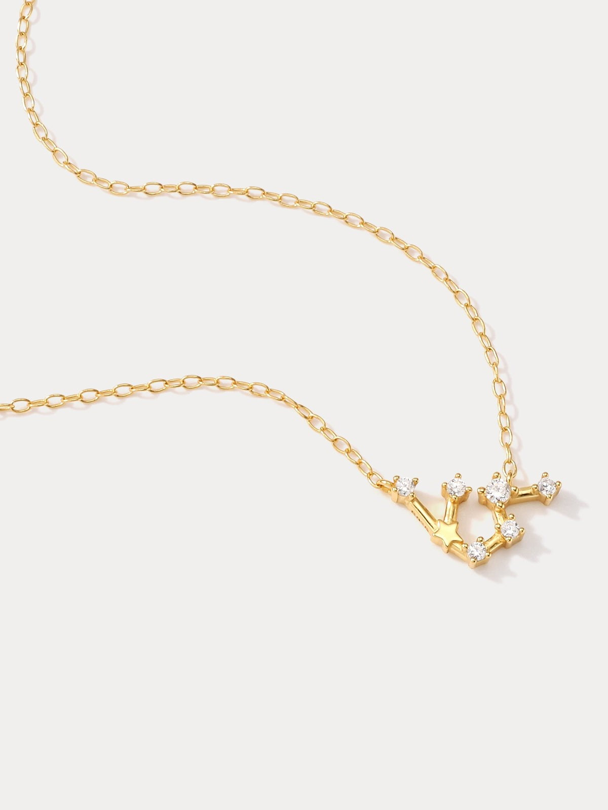 A dainty gold necklace featuring Aquarius constellation star sign displayed on a white surface.