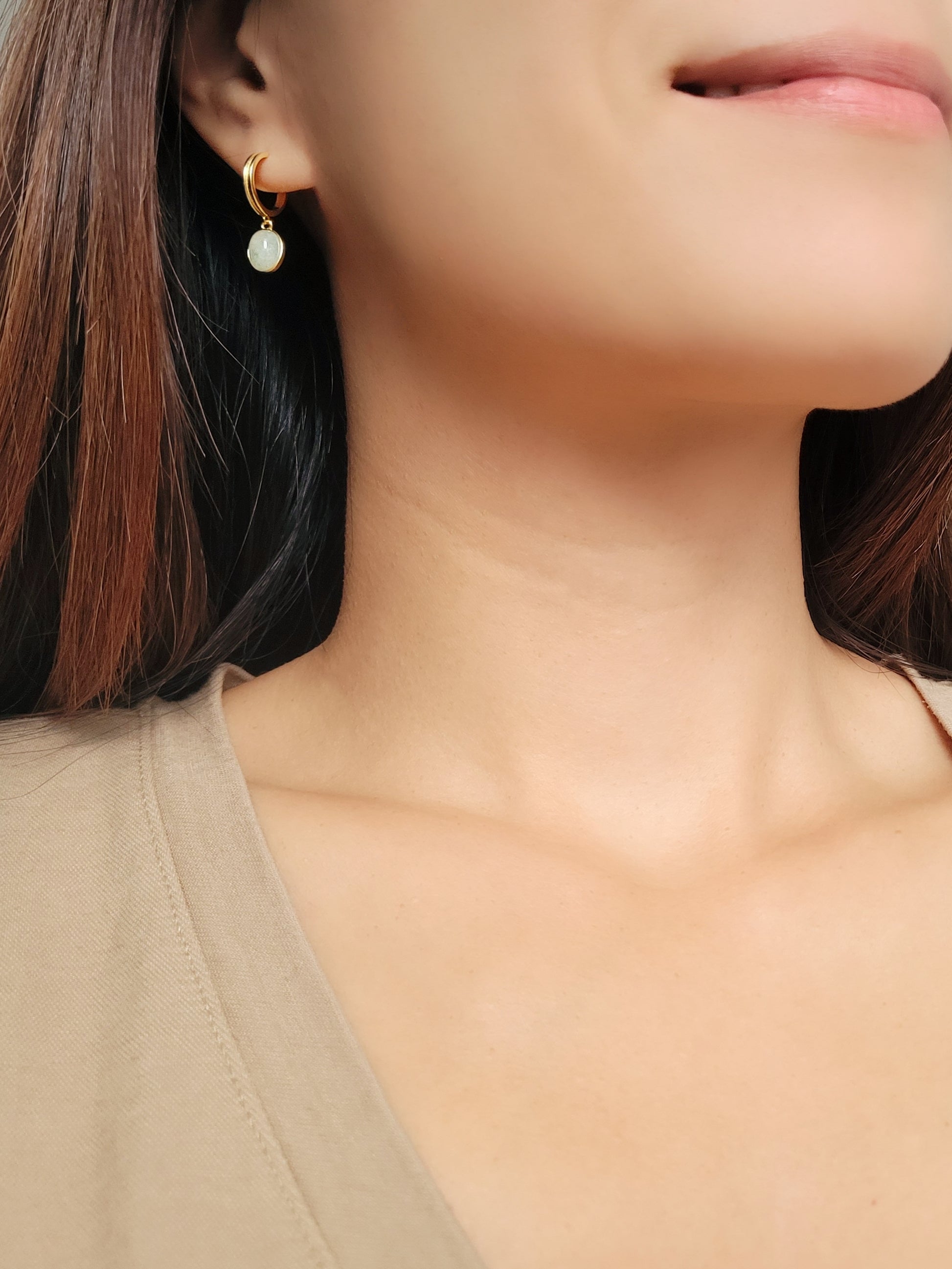 A woman showcases elegant gold earrings featuring stunning green aventurine stones, highlighting natural beauty and style. 
