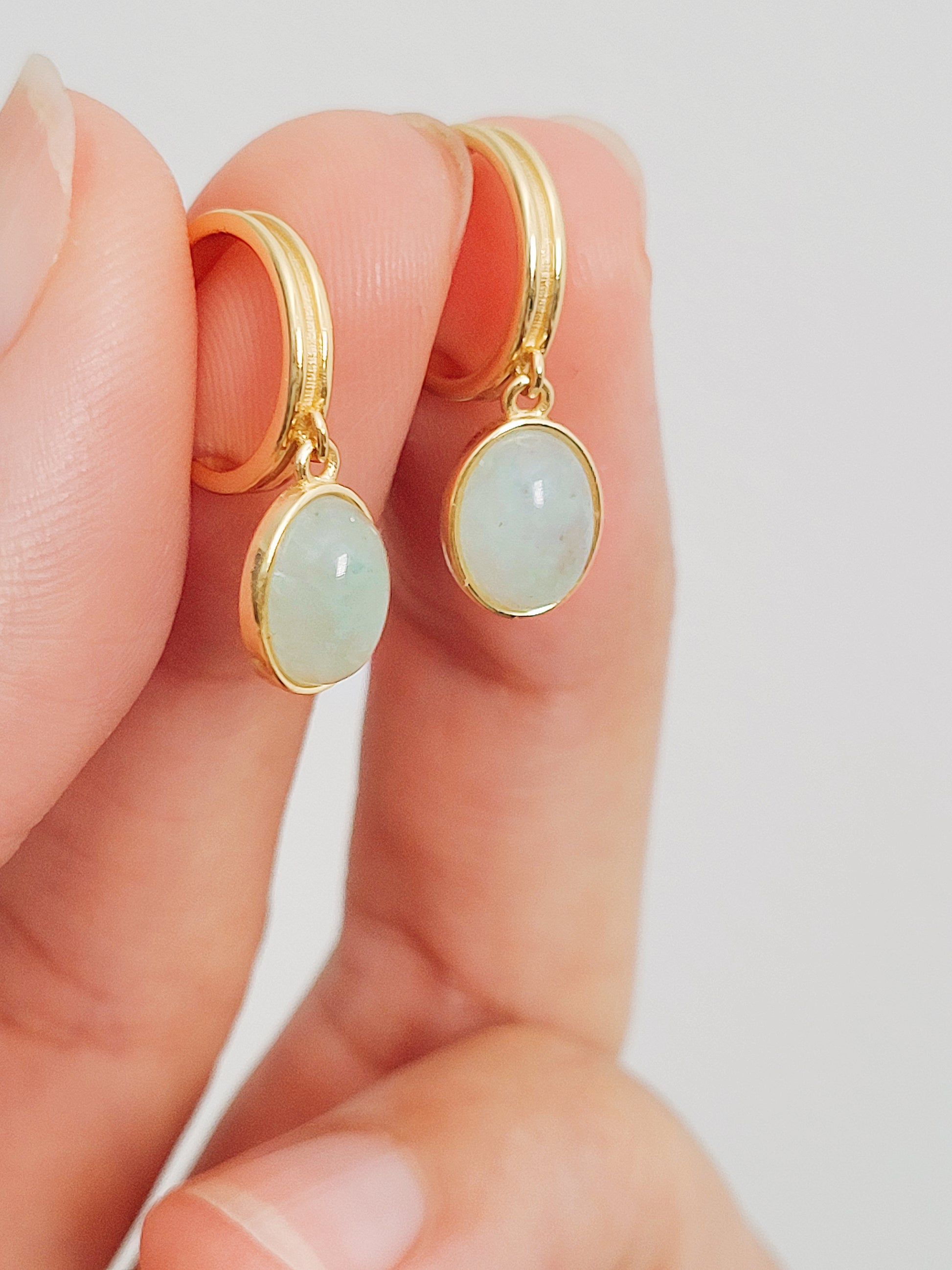 A woman's hand exquisite gold earrings adorned with vibrant green aventurine, emphasizing the allure of natural gemstones.