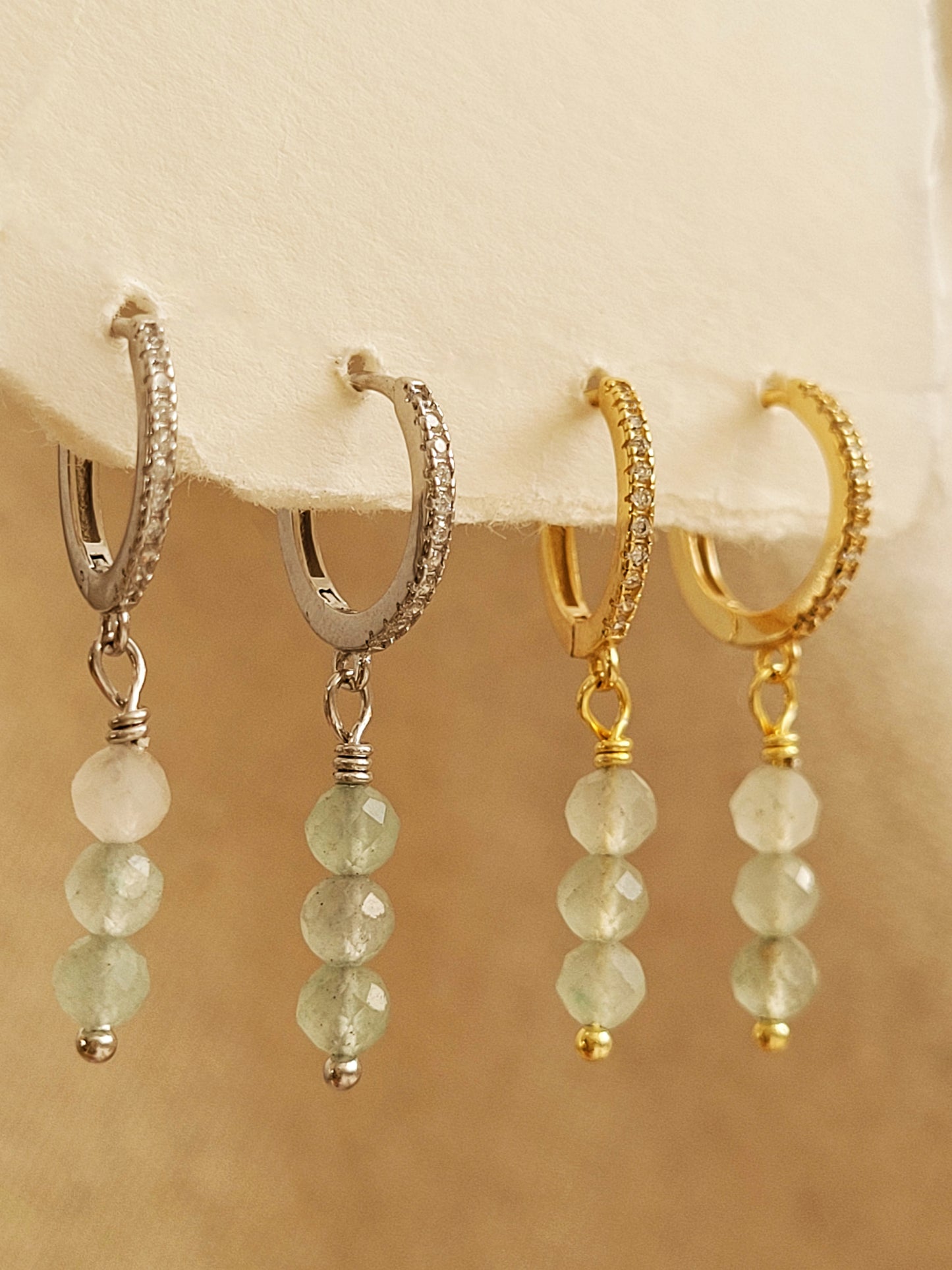 Set of dainty gold and silver aventurine drop earrings on a beige background.