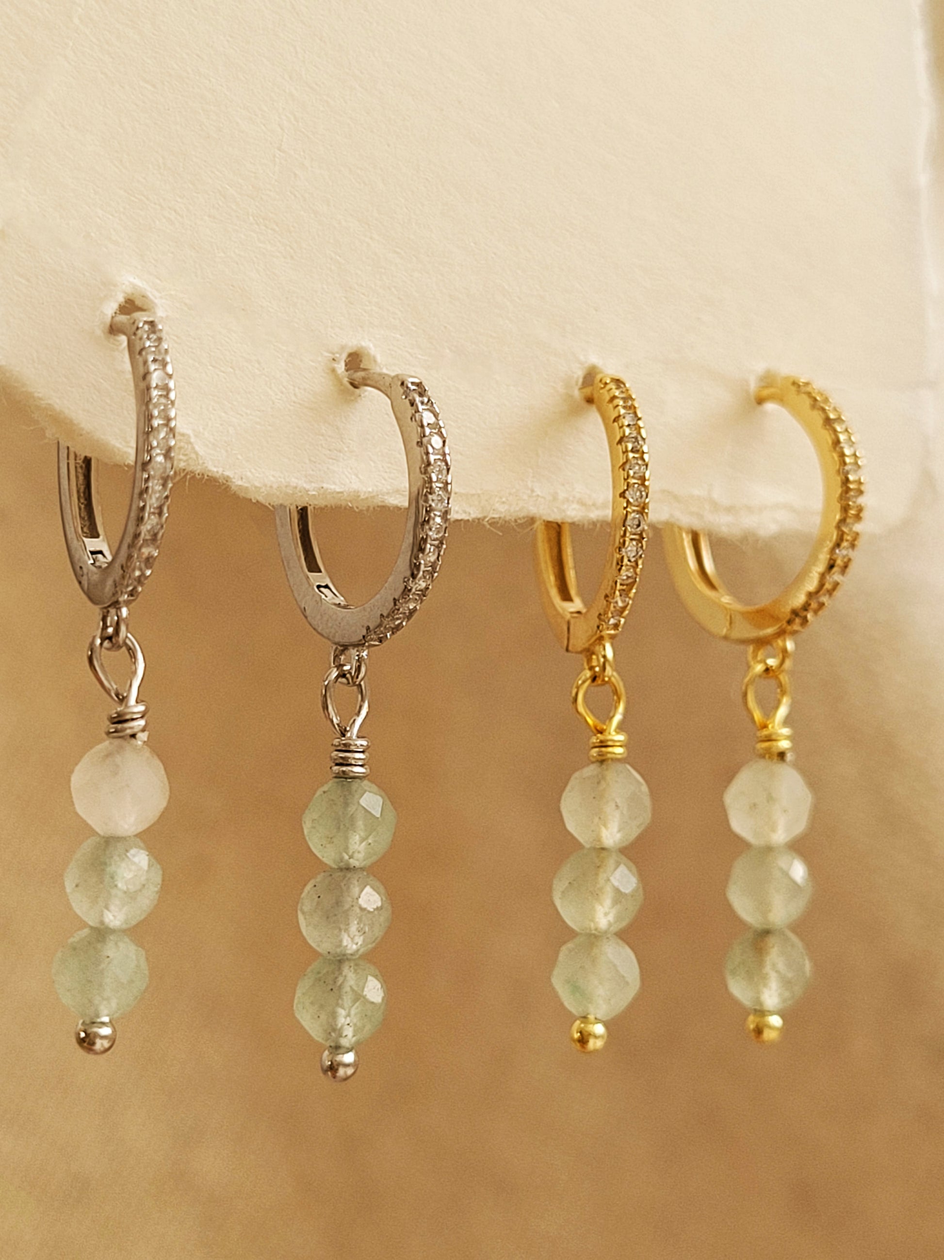 Set of dainty gold and silver aventurine drop earrings on a beige background.