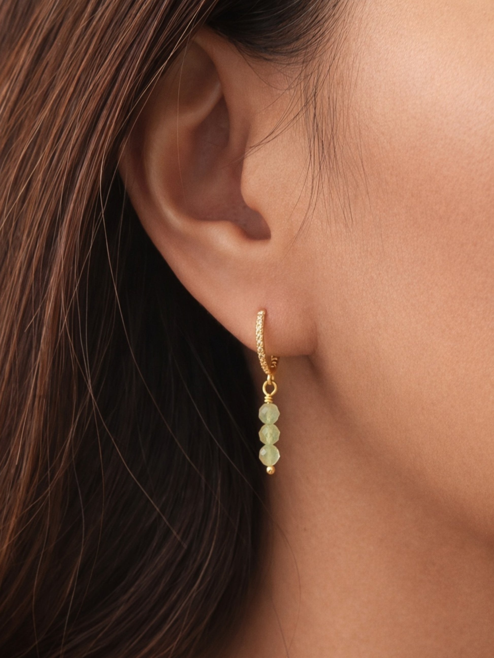 Model wearing dainty green aventurine drop earrings on gold huggie hoops.