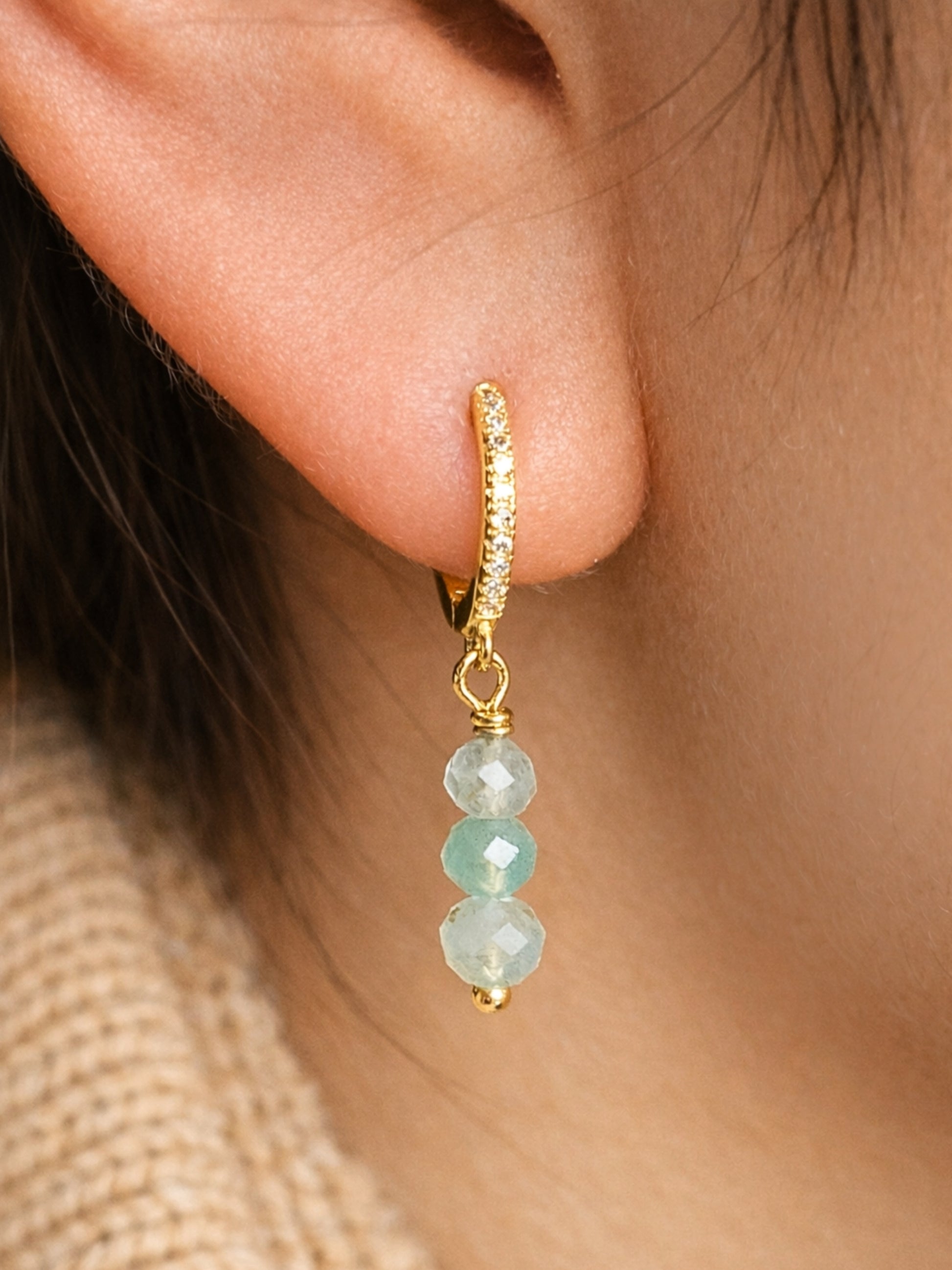 Gold hoop earring with green jade gemstones worn by a woman