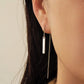 Close-up of a girl wearing a minimalist dangling silver bar earring with a neutral background