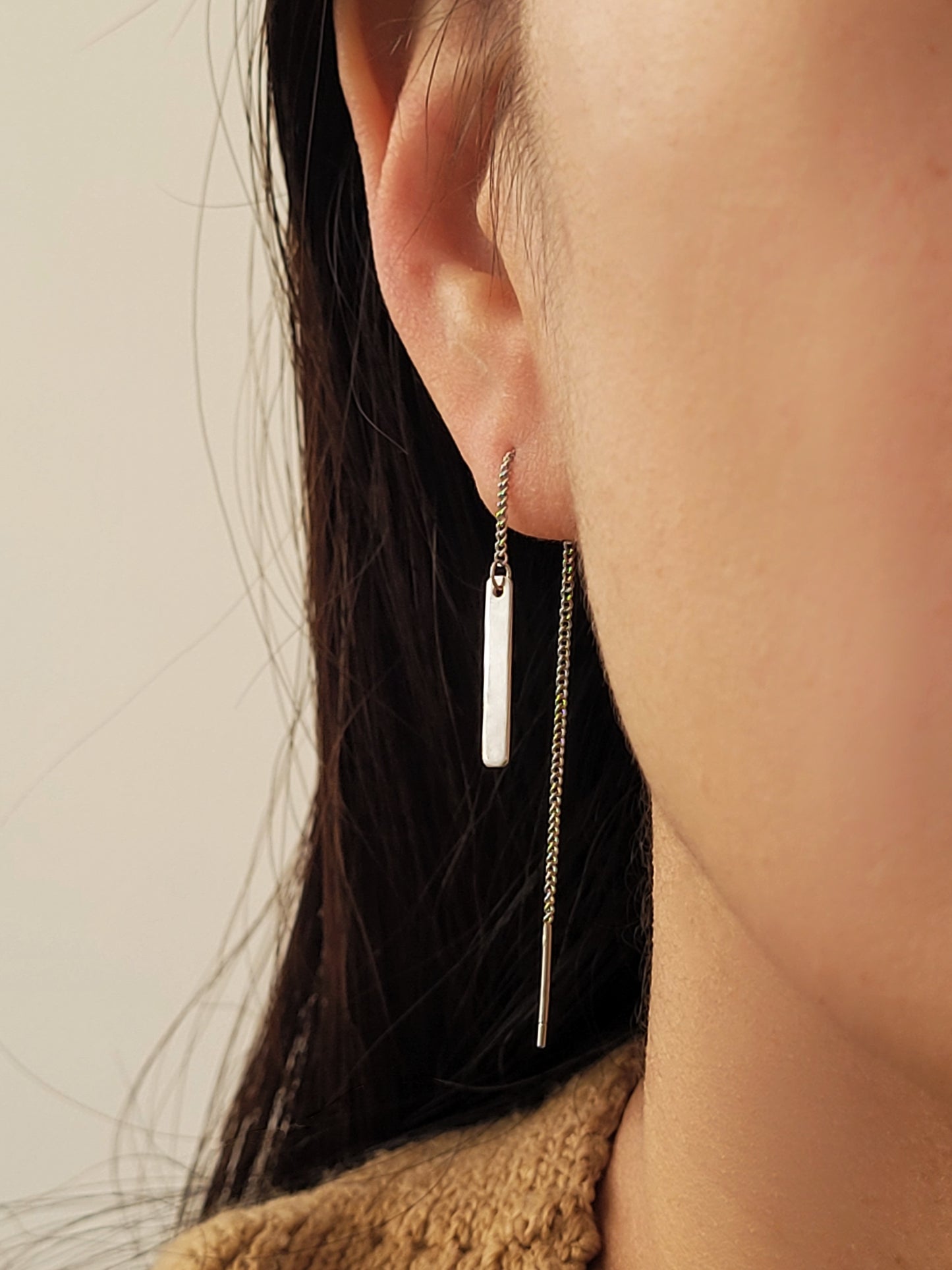 Close-up of a girl wearing a minimalist dangling silver bar earring with a neutral background
