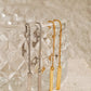 Long geometric ear Threaders in gold and silver hang on a glass.