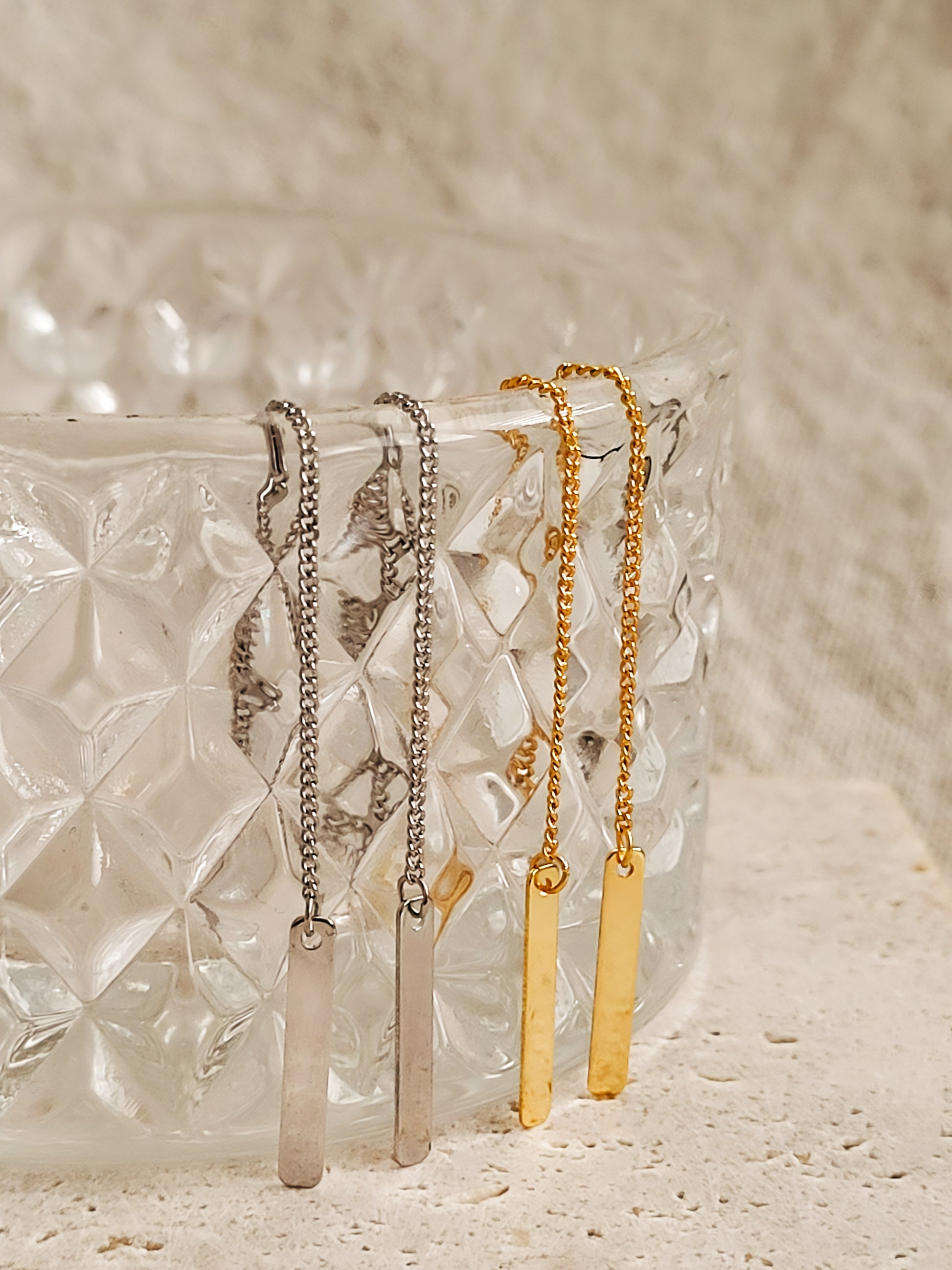 Long geometric ear Threaders in gold and silver hang on a glass.