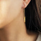 Close-up of a simple minimal gold threader earring worn by a woman.
