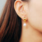 Close-up of a freshwater pearl dangling earring in gold on a woman’s ear.