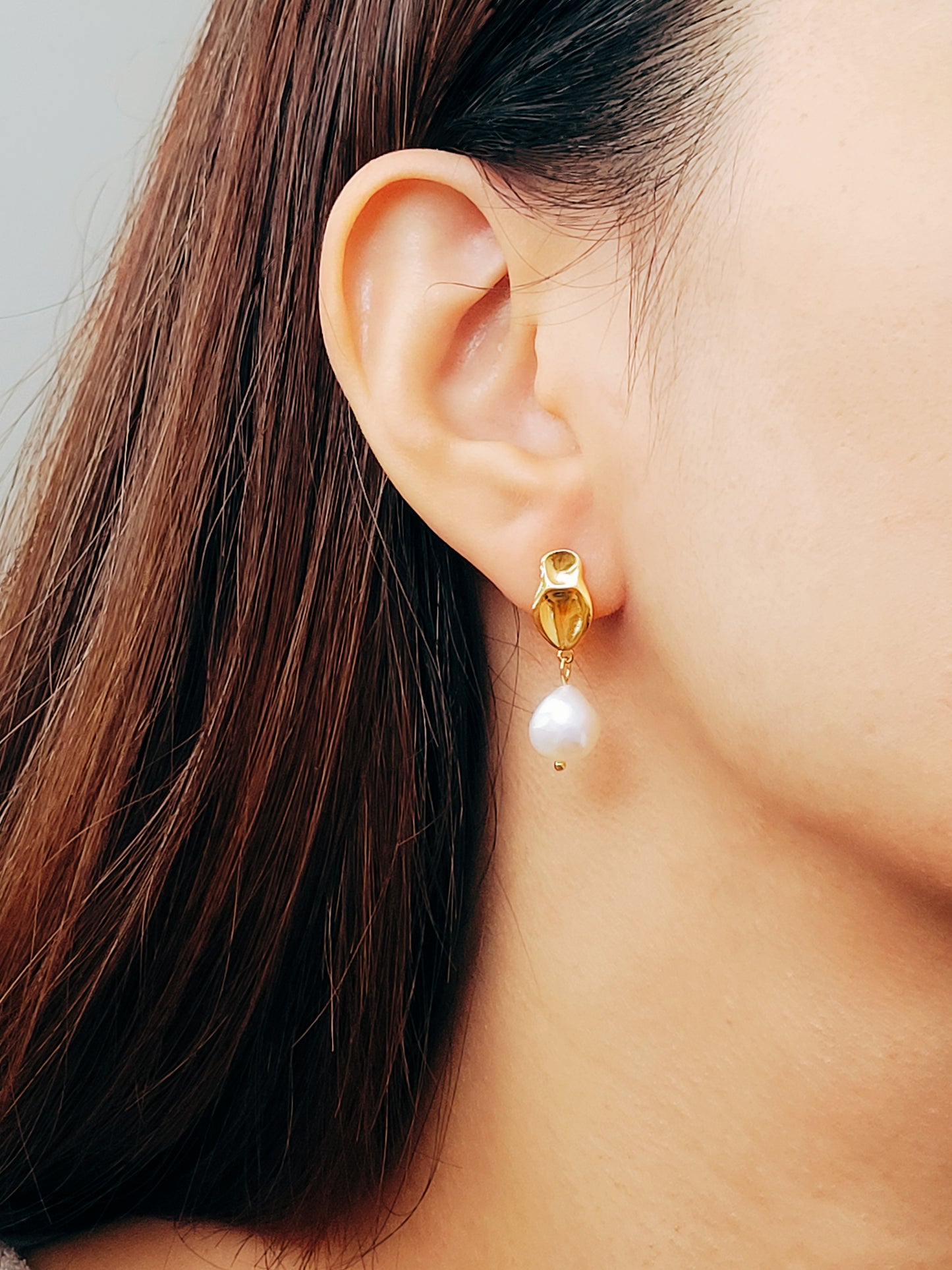 Close-up of a freshwater pearl dangling earring in gold on a woman’s ear.