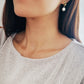 Gold earrings with a dangling baroque pearl drop, worn by a woman.
