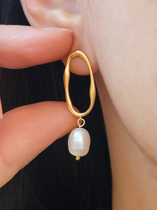 Close-up of baroque pearl drop earrings in gold.