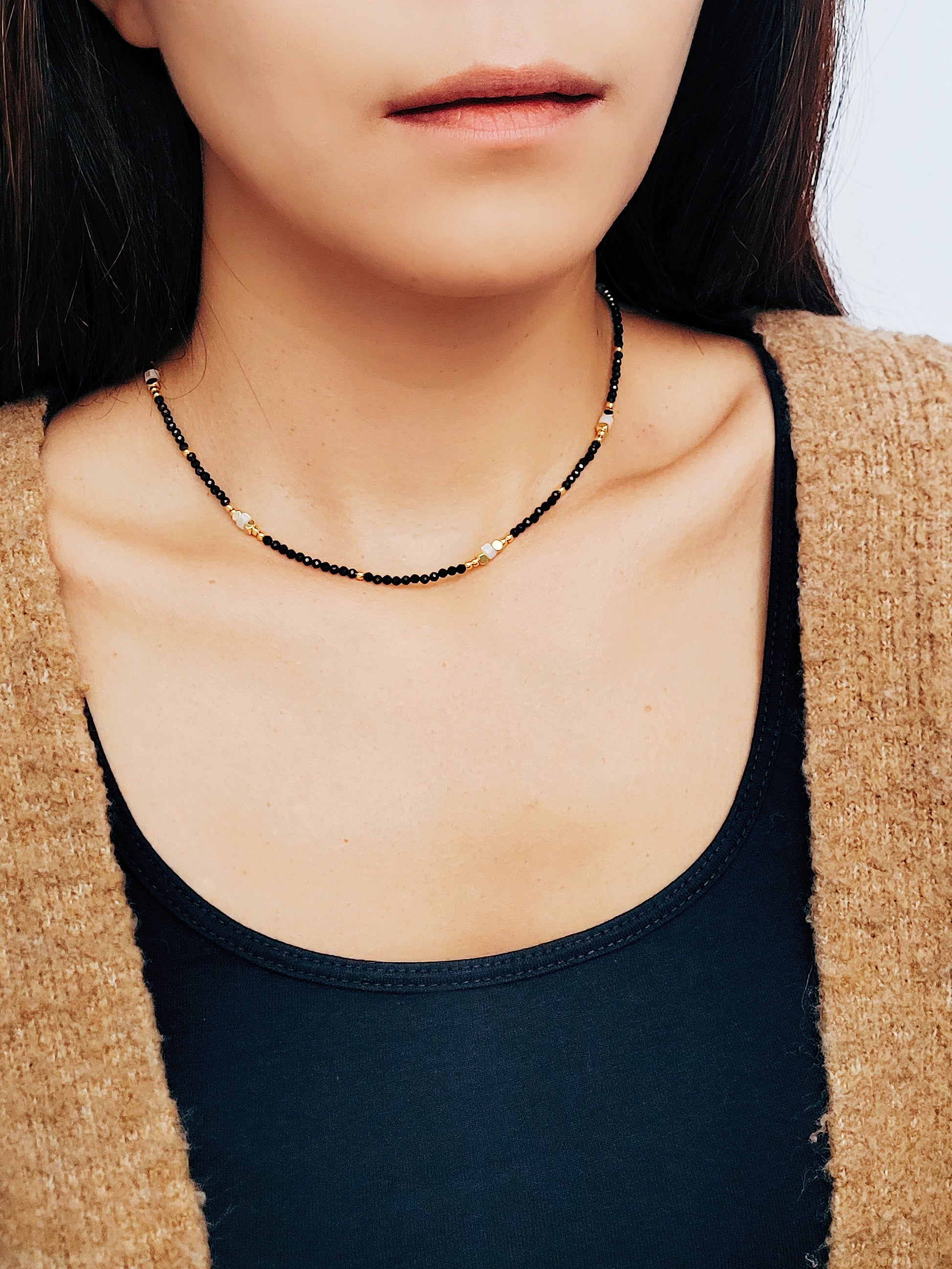 A woman elegantly shows her black spinel beaded necklace, adorned with gold and white beads radiating sophistication and refined taste.