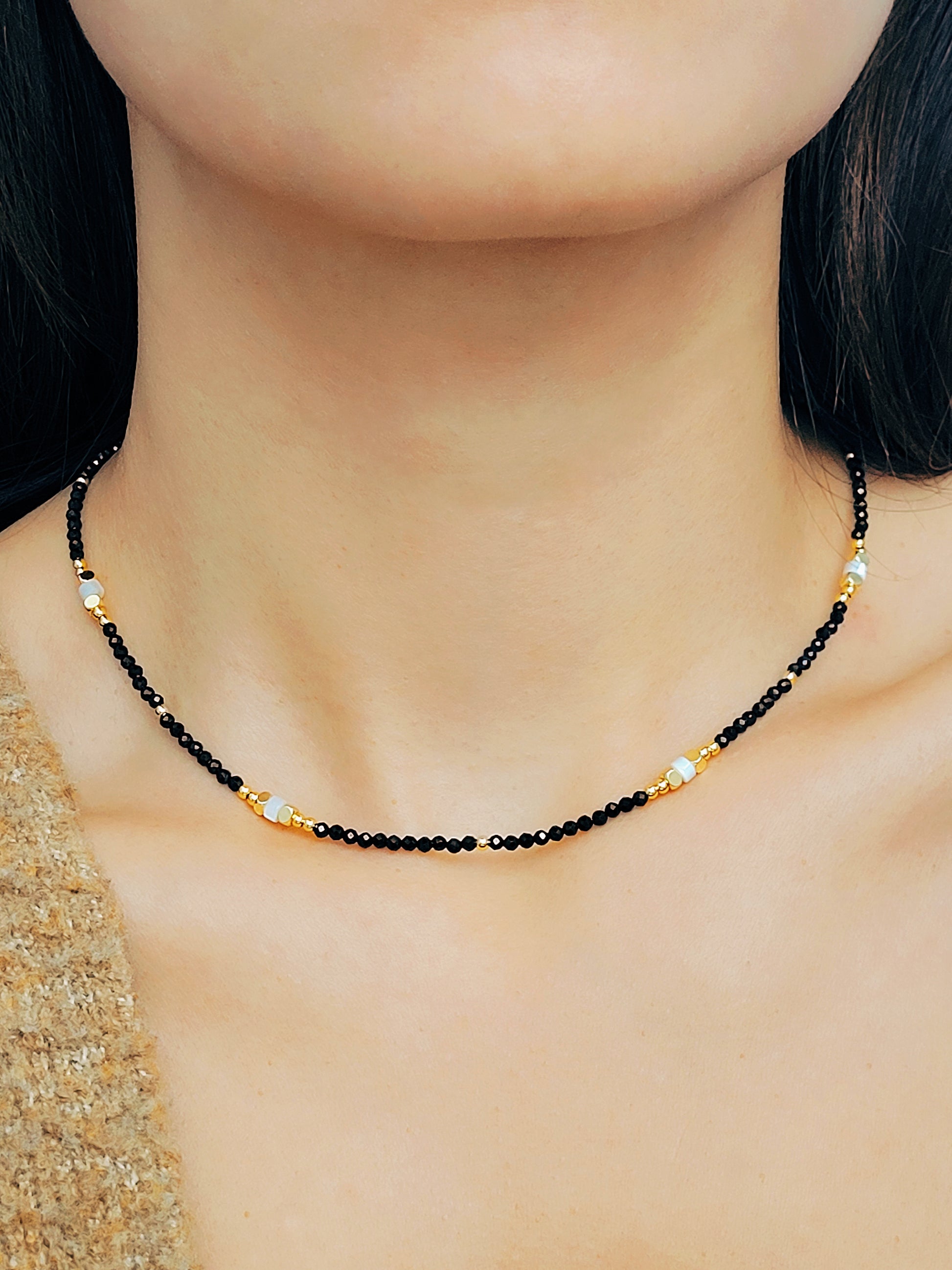 A woman elegantly shows her black spinel beaded necklace, adorned with gold and white beads radiating sophistication and refined taste.