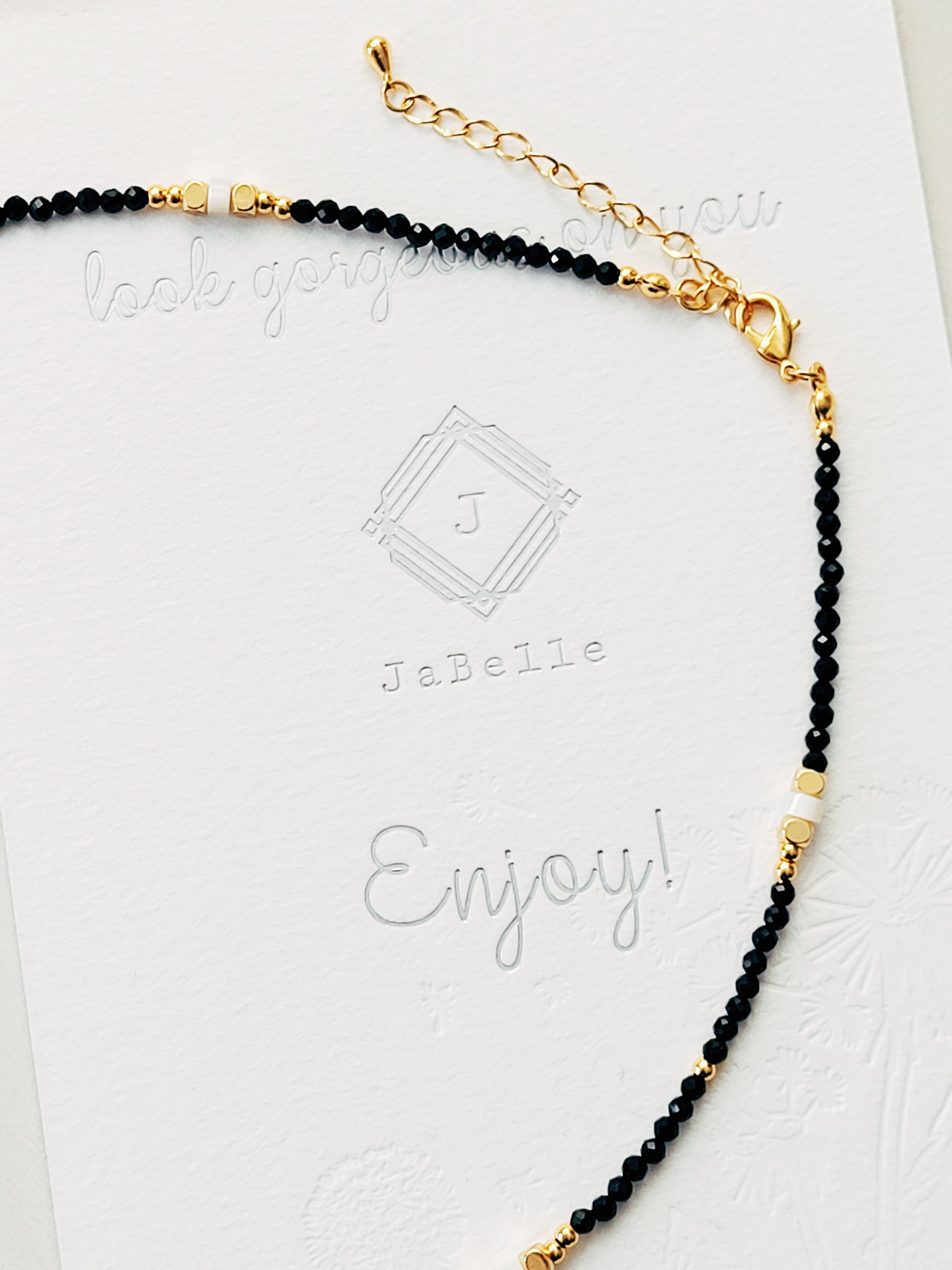 A Black Spinel Beaded Necklace with gold beads and mother of pearl beads is displayed on a card.