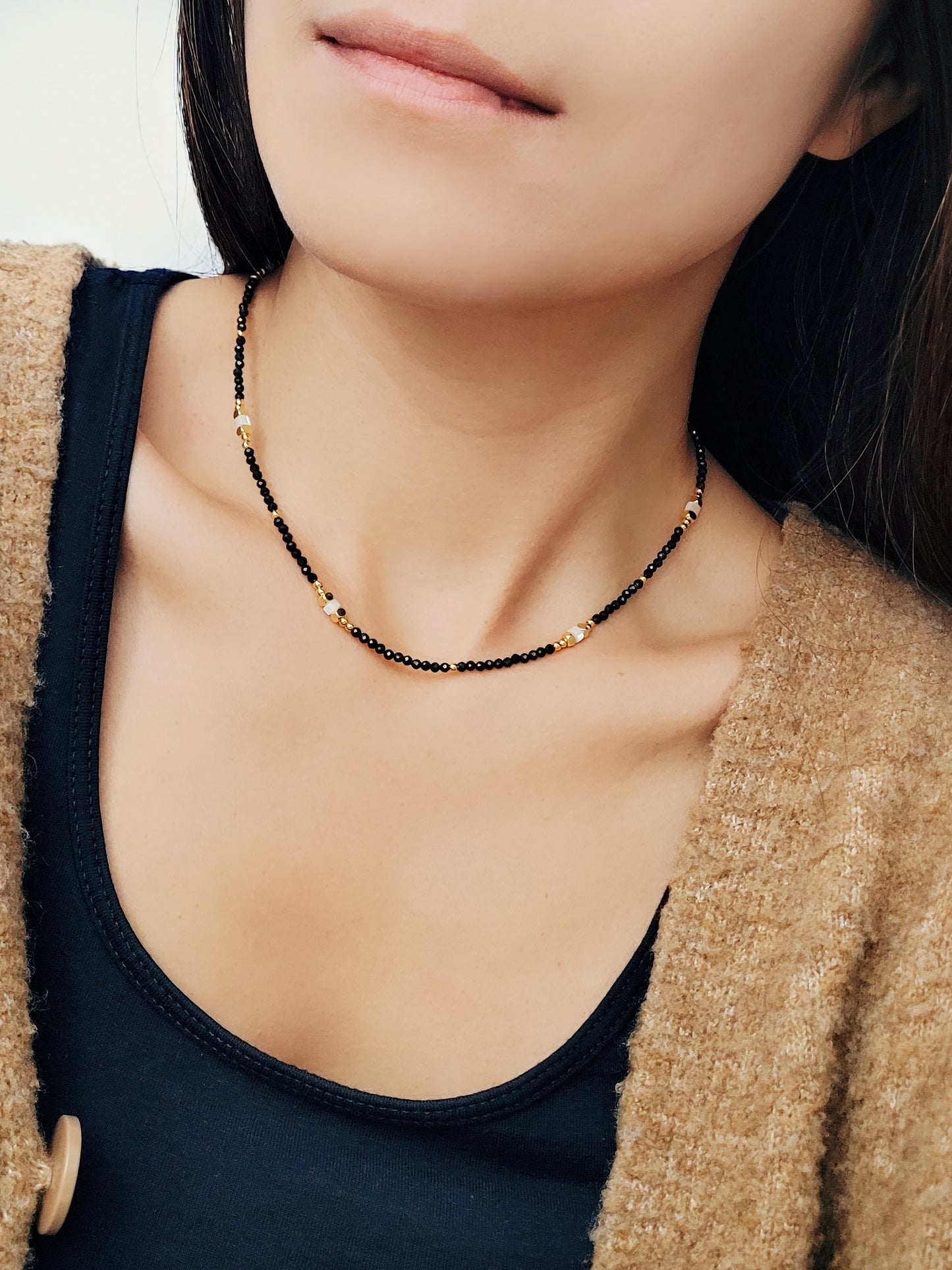 A woman delicately showcases her chic black spinel beaded necklace, embodying elegance and timeless style.