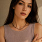 Portrait of a female model with long brunette hair wearing a dainty black spinel choker necklace. The delicate necklace features tiny, faceted black beads accented by small 22k gold vermeil beads, resting gracefully above her collarbone. She is styled in a ribbed, sleeveless mauve-taupe knit top against a warm, neutral background.