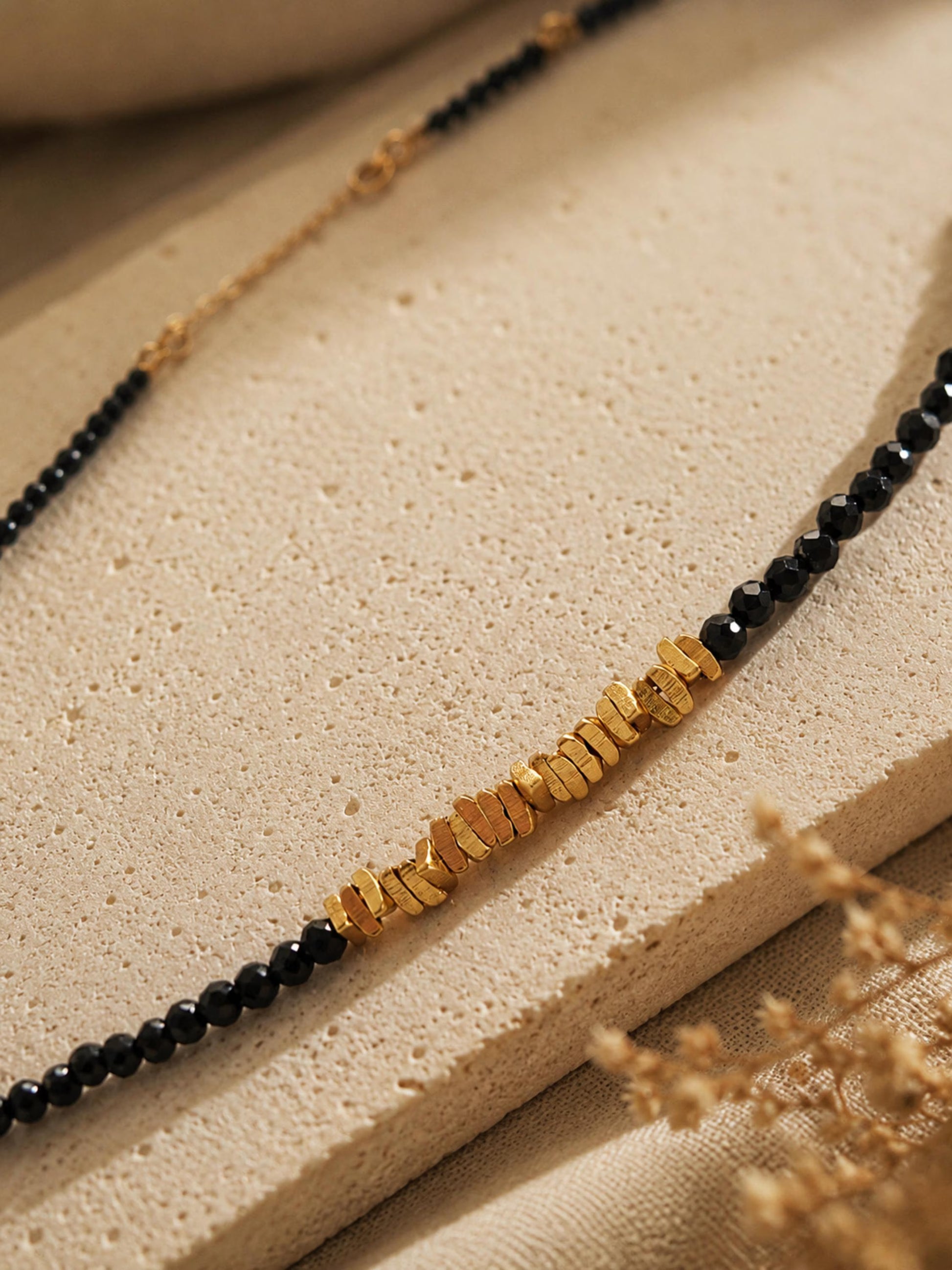Detailed view of a dainty black spinel gemstone choker necklace with organic 22k gold vermeil nugget displayed on a stone surface.