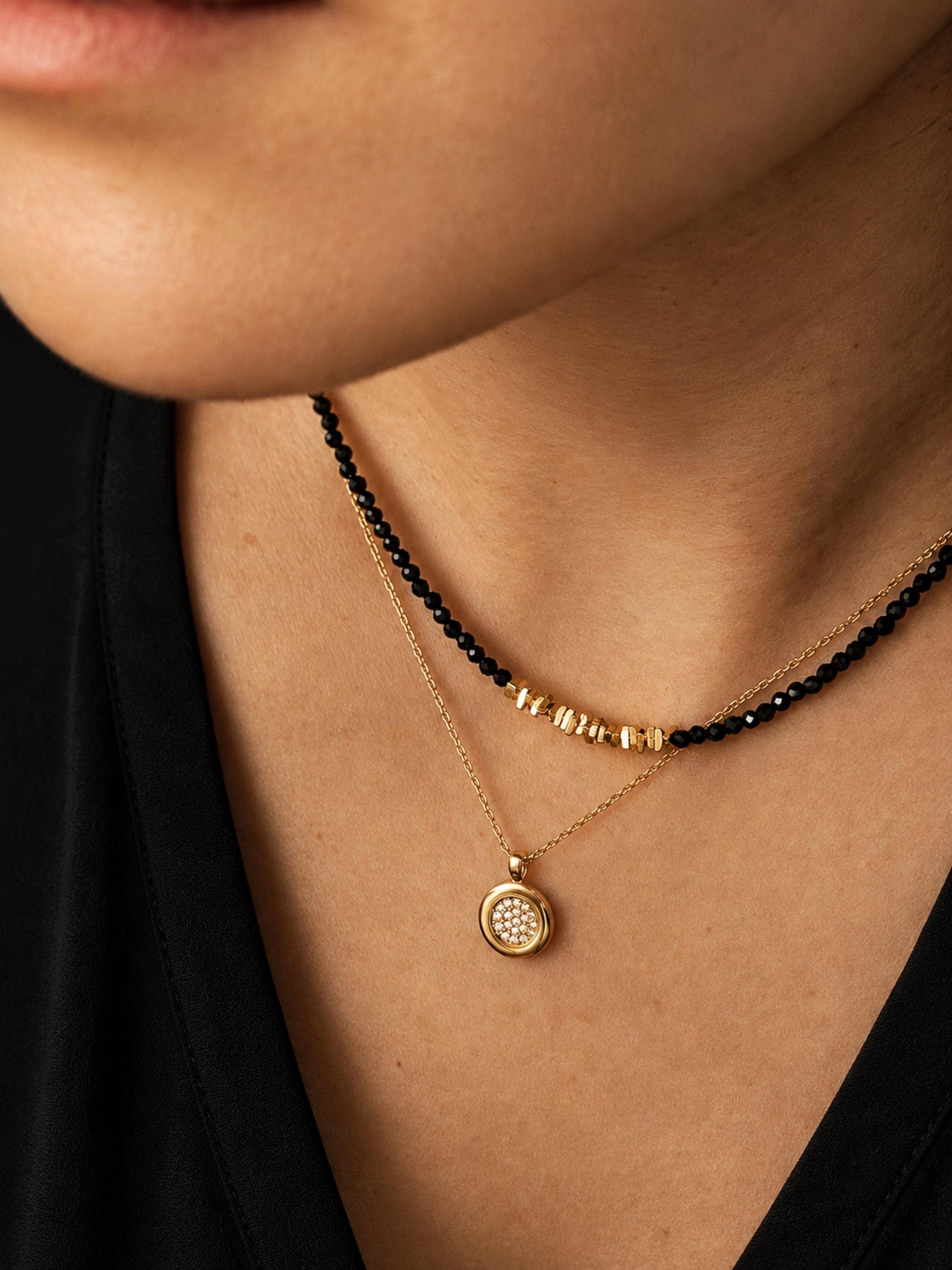 A close-up of a woman wearing a delicate 2mm black spinel beaded choker necklace featuring a center accent cluster of organic, textured 22k gold vermeil nuggets layered with a round diamond pendant necklace.