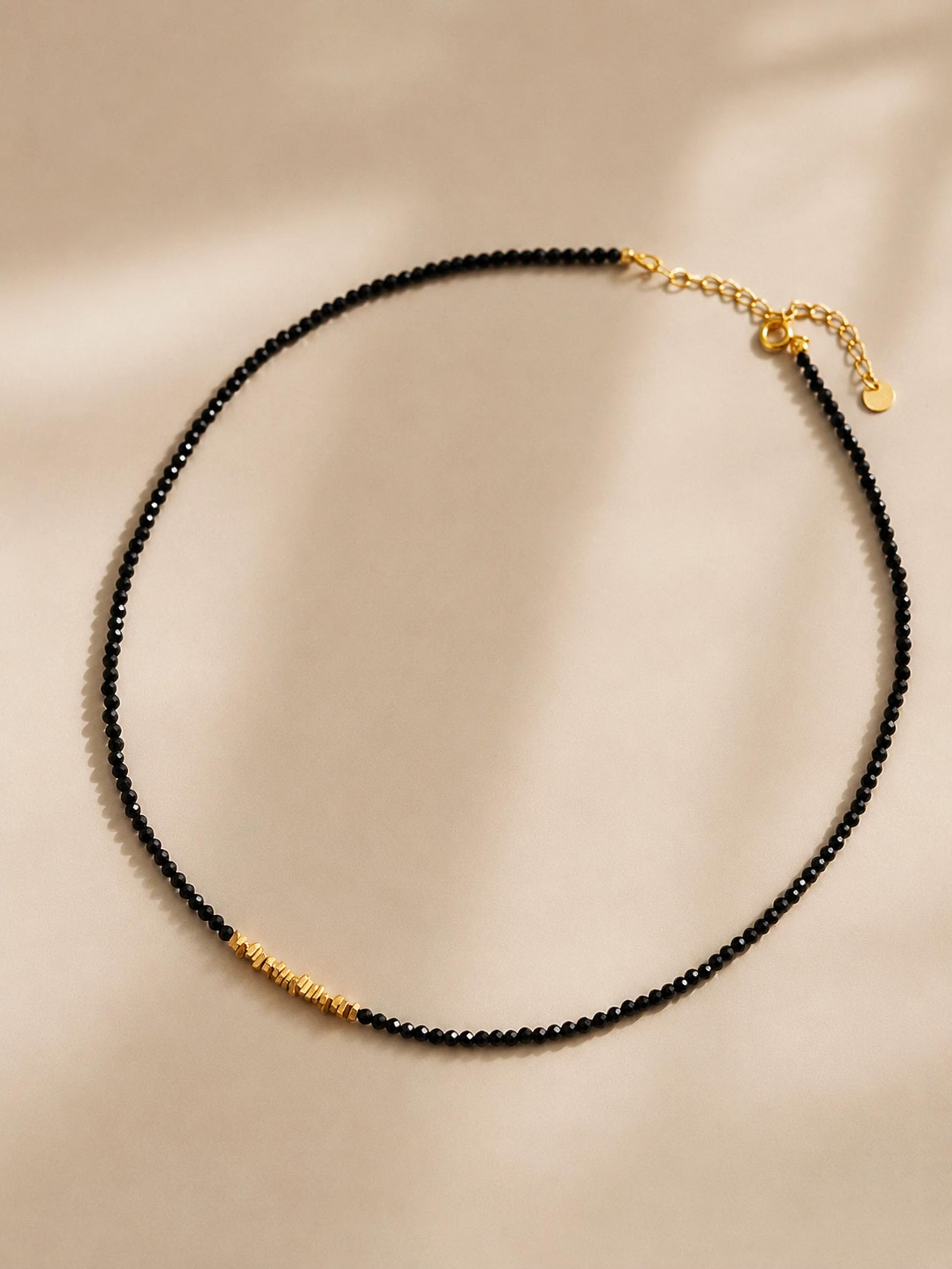 A dainty black spinel gemstone choker necklace with organic 22k gold vermeil nugget displayed on a white surface. 