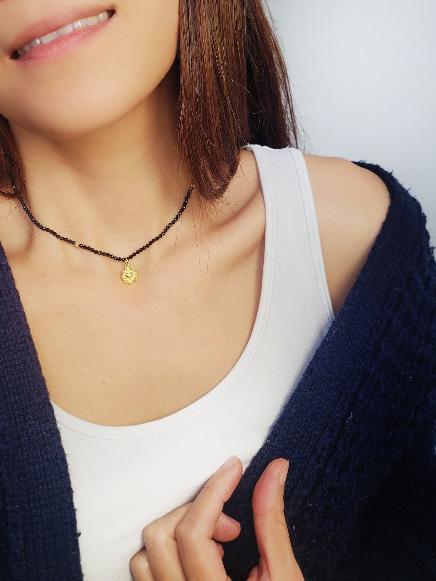 A woman gracefully wears her elegant black spinel beaded necklace with a beautiful gold heart charm, showcasing its stylish allure and sophistication.