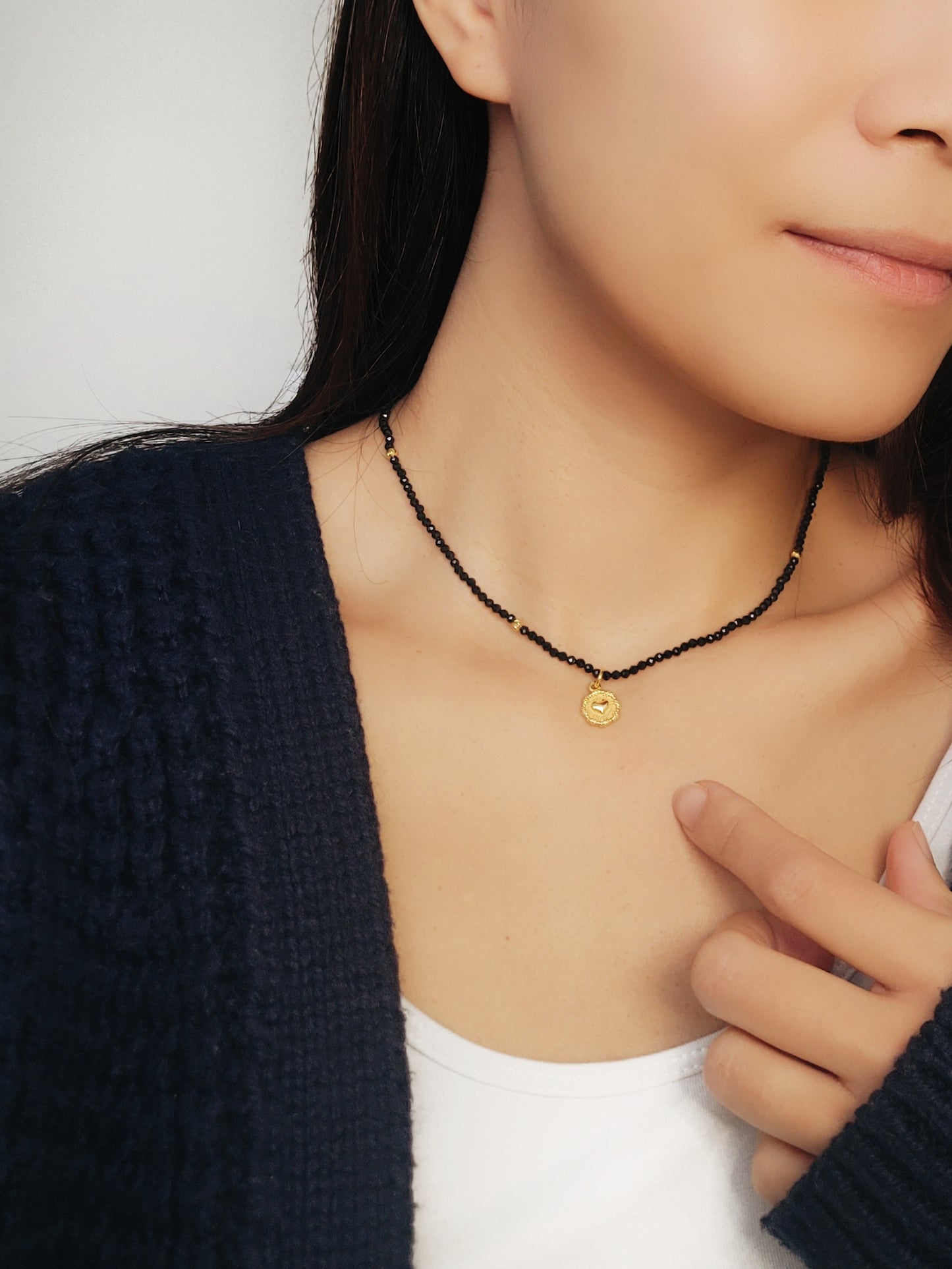 A woman elegantly shows her black spinel beaded necklace, adorned with gold and white beads radiating sophistication and refined taste.