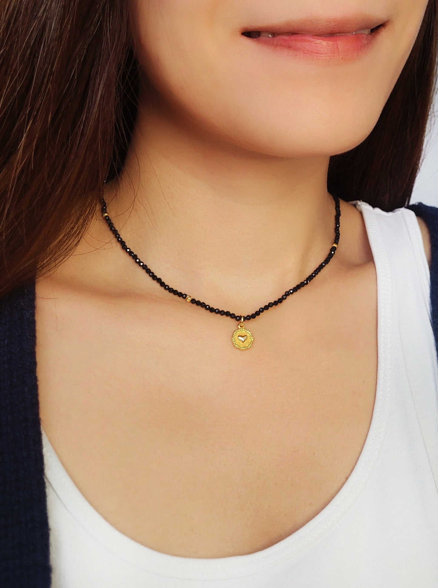 A woman elegantly shows her black spinel beaded necklace with gold coin pendant. Crafted in gold plated 925 sterling silver radiating sophistication and refined taste.