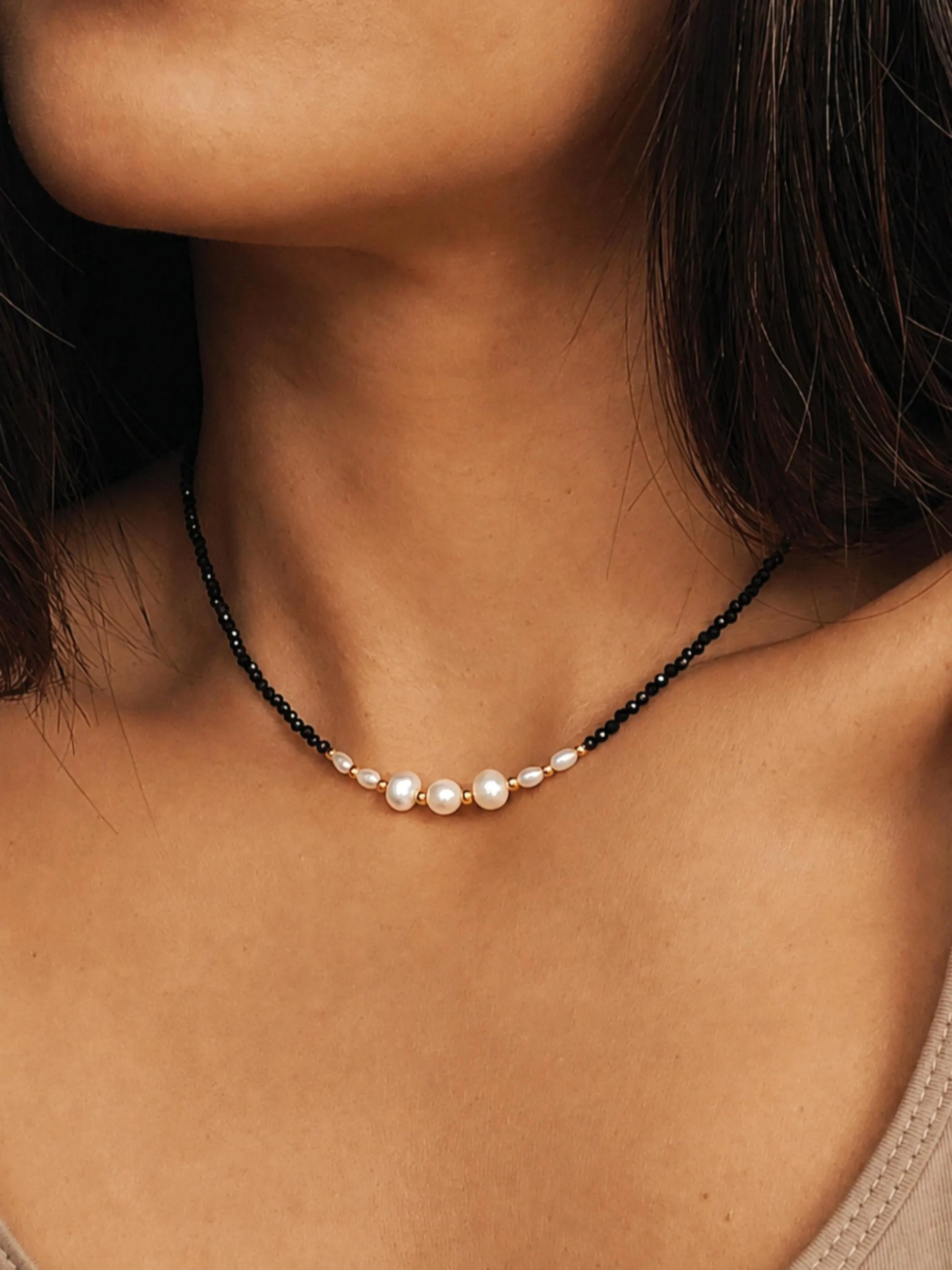 Black spinel and freshwater pearl choker necklace with 18k gold plated sterling silver accents, worn by a woman. Delicate pearl and gemstone necklace for everyday wear, layering and elegant bridal jewellery.