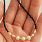 Close-up of a hand holding a black spinel beaded gemstone choker necklace with freshwater pearls again an aesthetic luxury beige background.