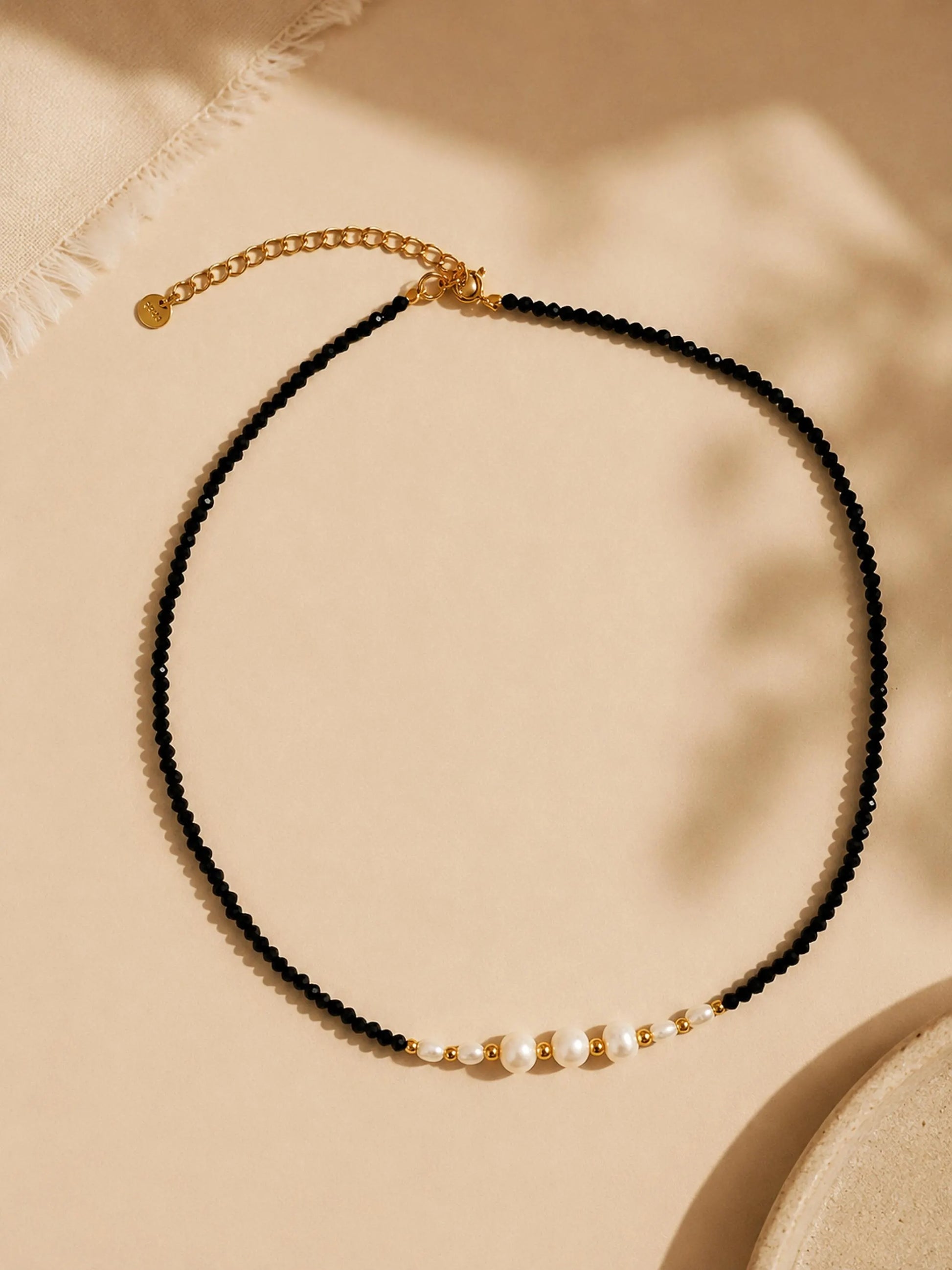 Black spinel gemstone choker necklace featuring freshwater pearls and 18k gold plated sterling silver beads, displayed on a neutral beige background. Minimalist pearl necklace for weddings, bridesmaids and everyday styling.