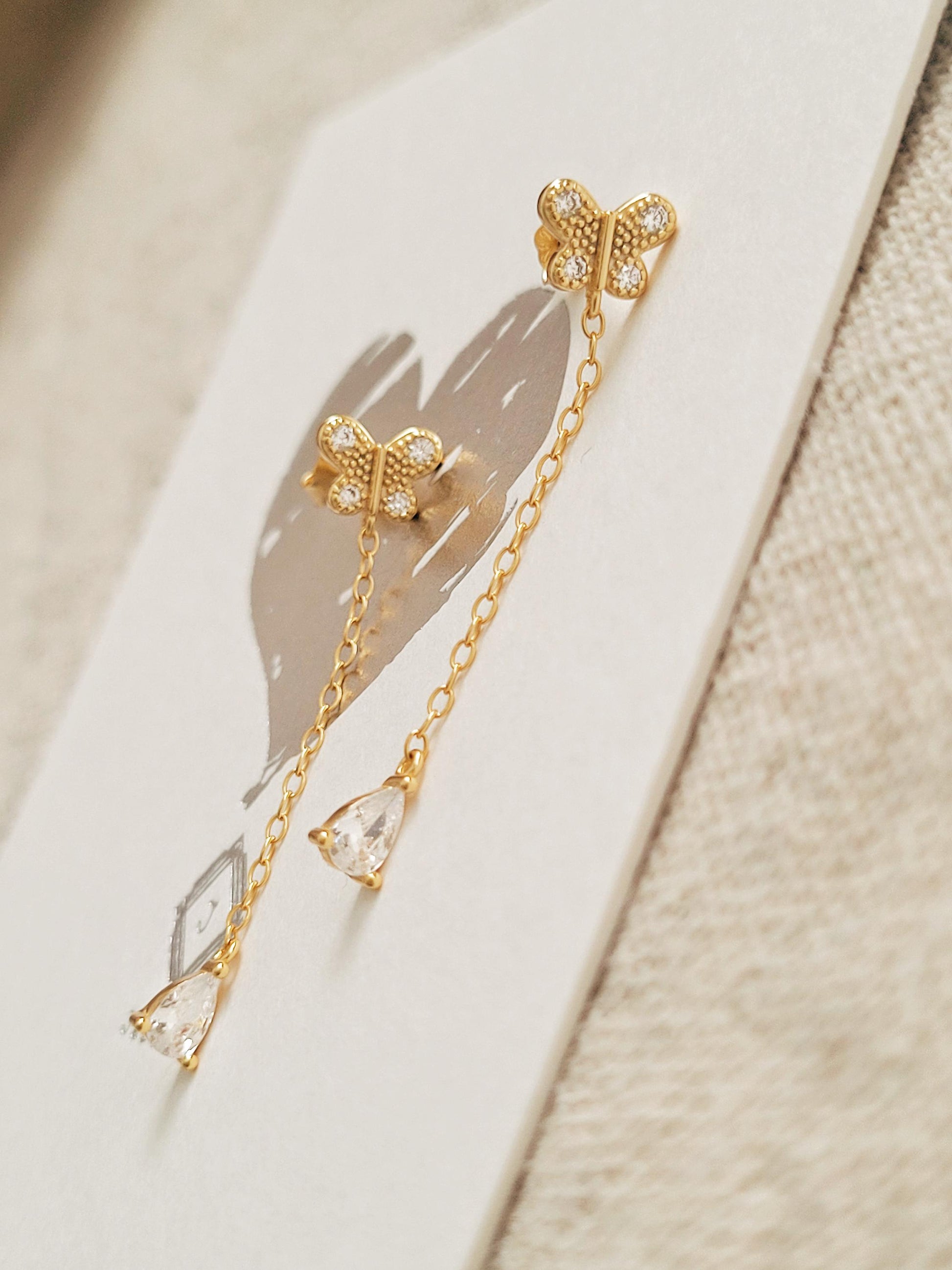 A pair of dainty gold butterfly earrings with long chain details on a white surface