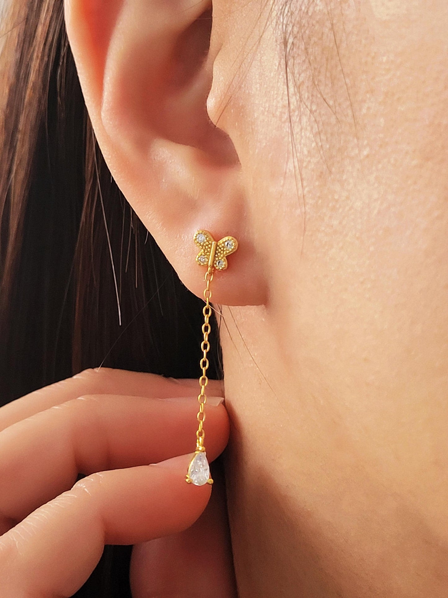 Dainty 18k gold vermeil butterfly stud earring with a delicate chain drop and sparkling pear-cut cubic zirconia stone worn on a model.