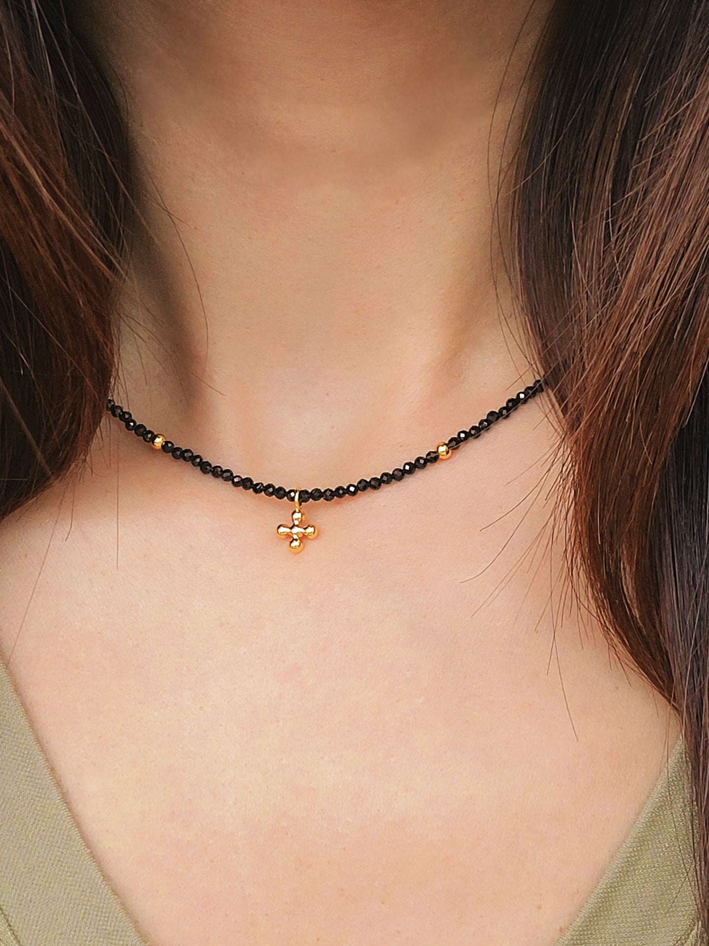 Close-up of a woman wearing an elegant black spinel beaded necklace with a mini clover pendant in gold.