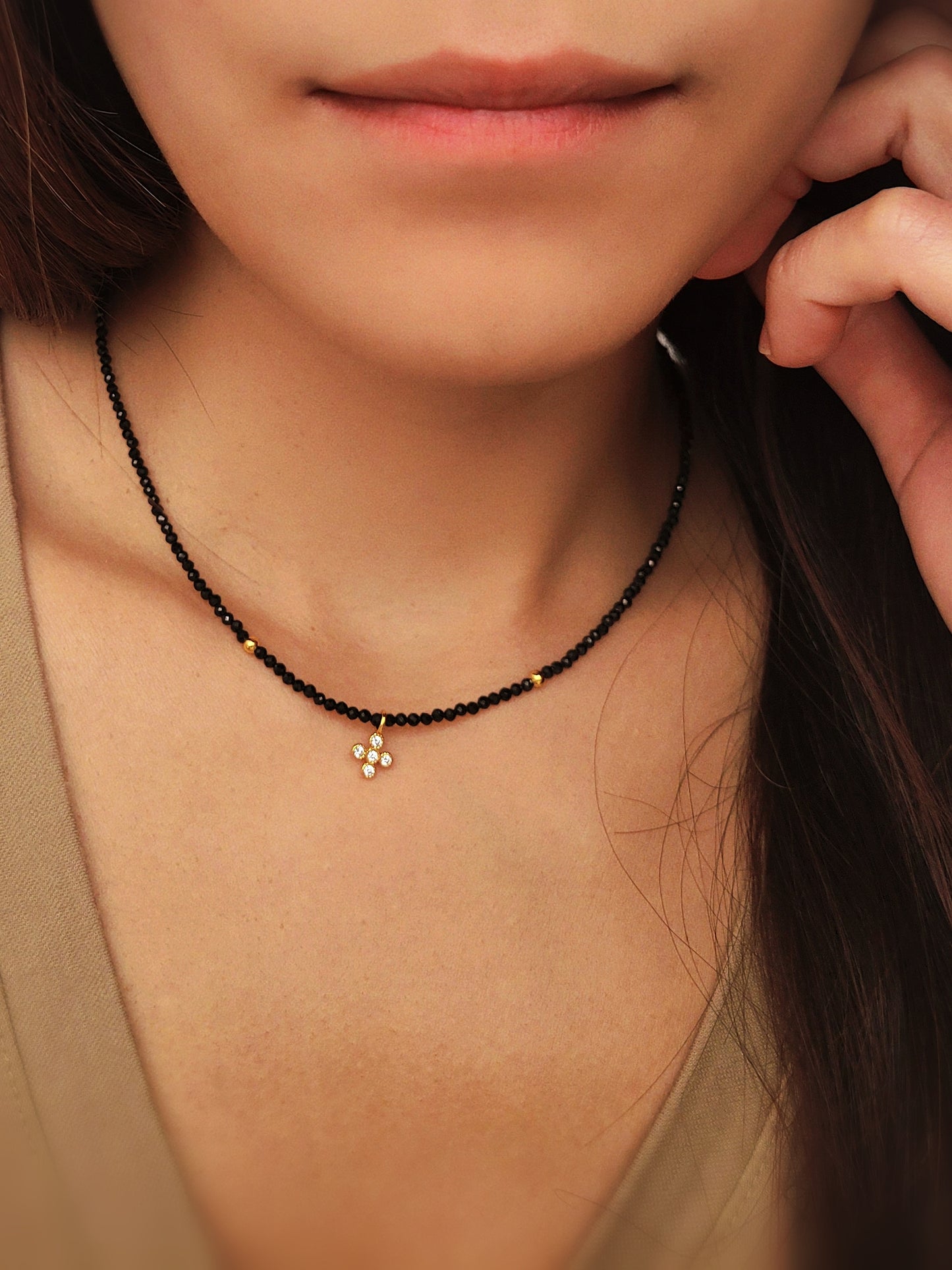 Close-up of a woman wearing an elegant black spinel beaded necklace with a mini clover pendant in gold.