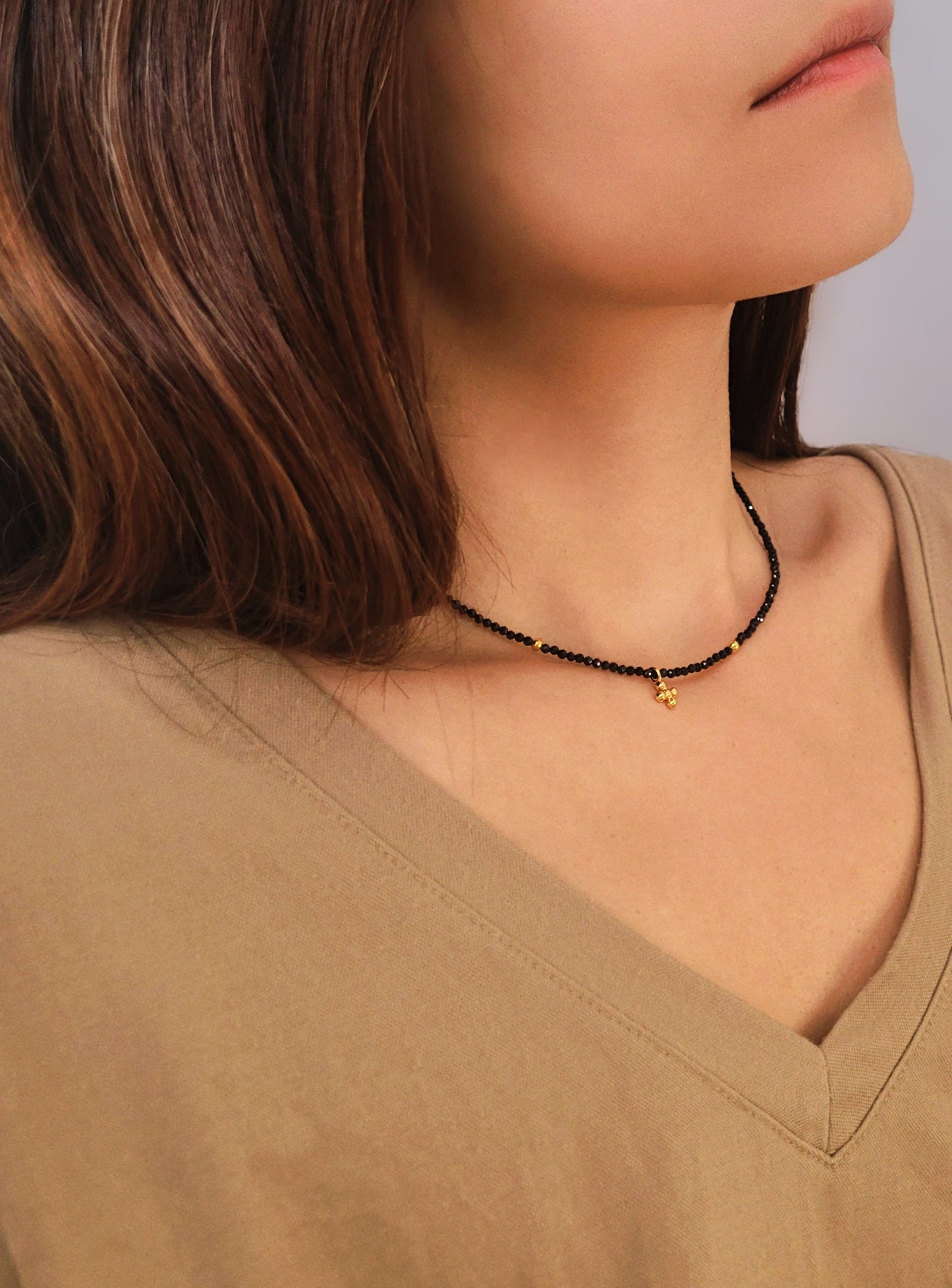 Close-up of a woman wearing an elegant black spinel beaded necklace with a mini clover pendant in gold.