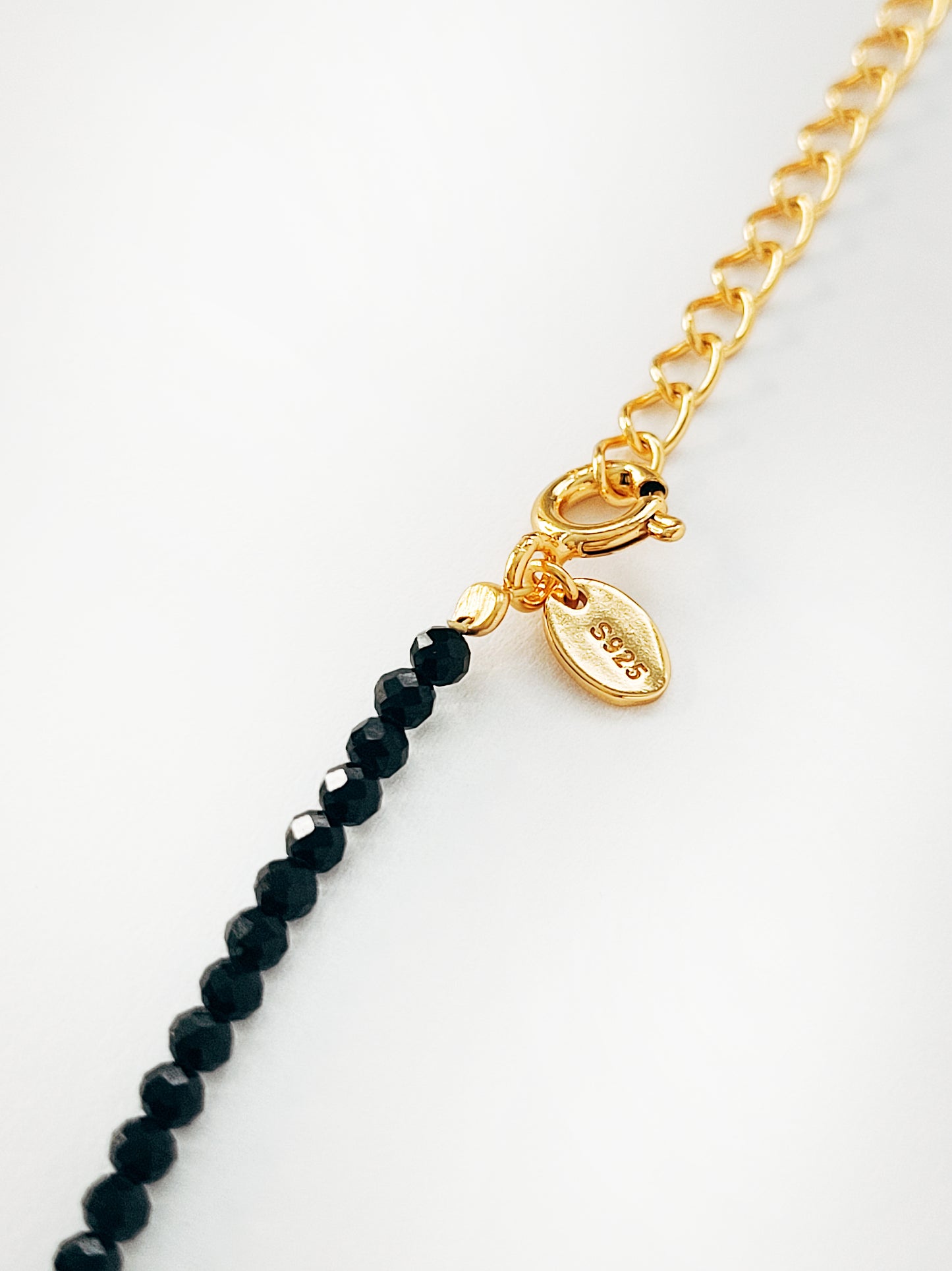 Close-up of the closure using spring ring on a natural black spinel gemstone choker necklace with S925 on a gold plated tag which means crafted in 925 sterling silver.