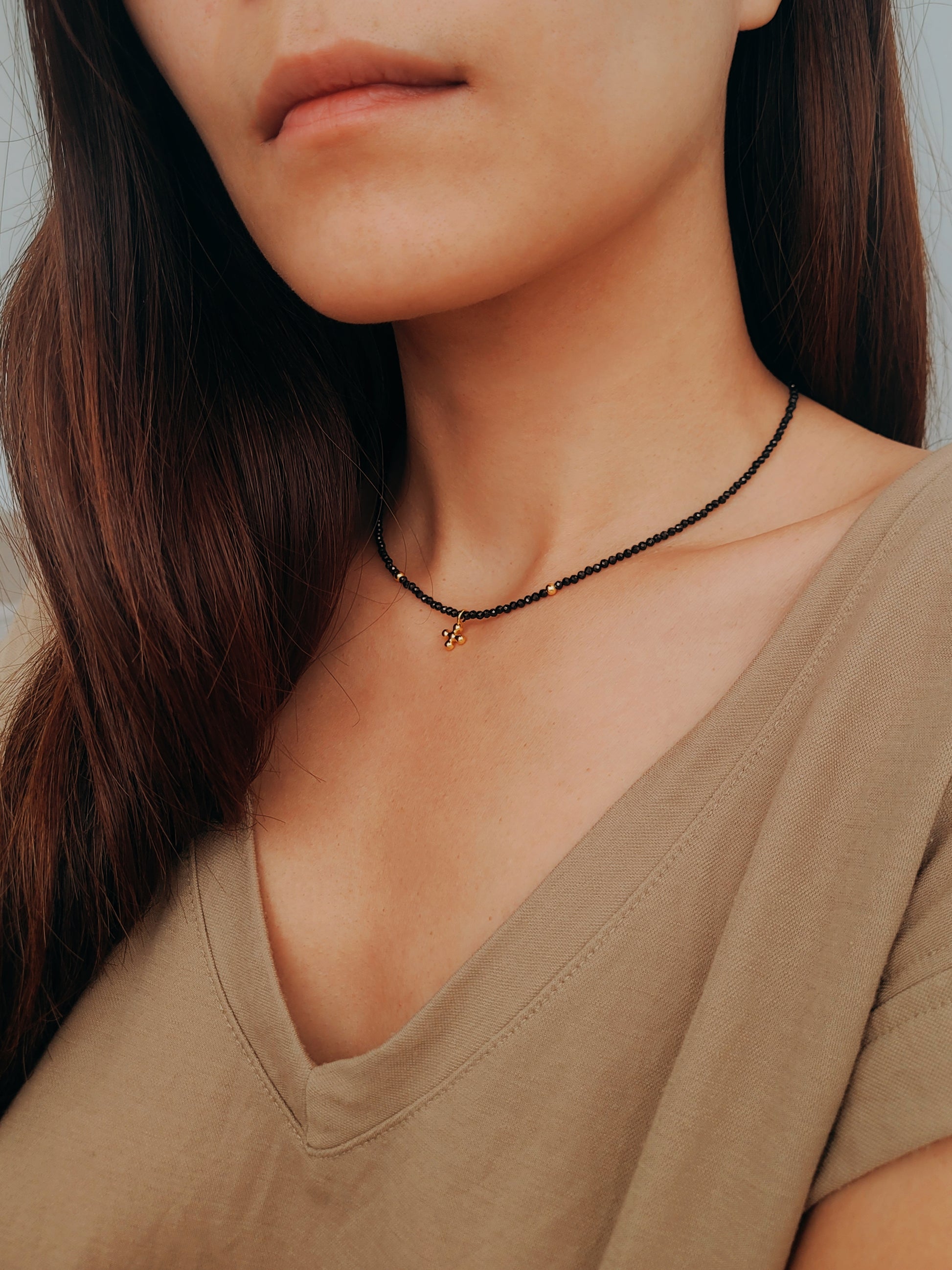 Close-up of a woman wearing an edgy black spinel beaded necklace with a mini clover pendant in gold.