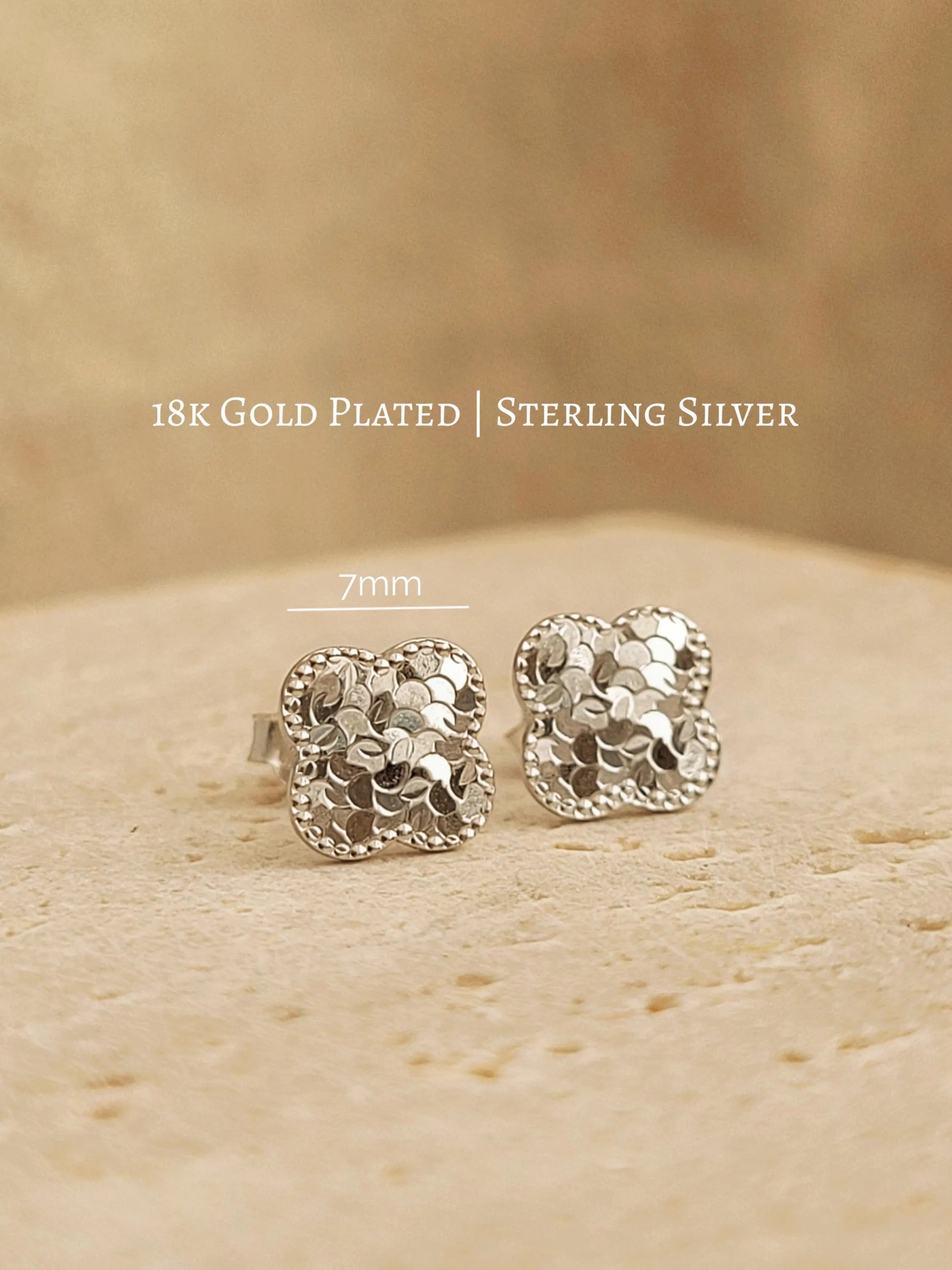 Close up of a pair of dainty clover stud earrings in 925 sterling silver, showing the intricate textured detail on an aesthetic beige stone surface, perfect gift for wife