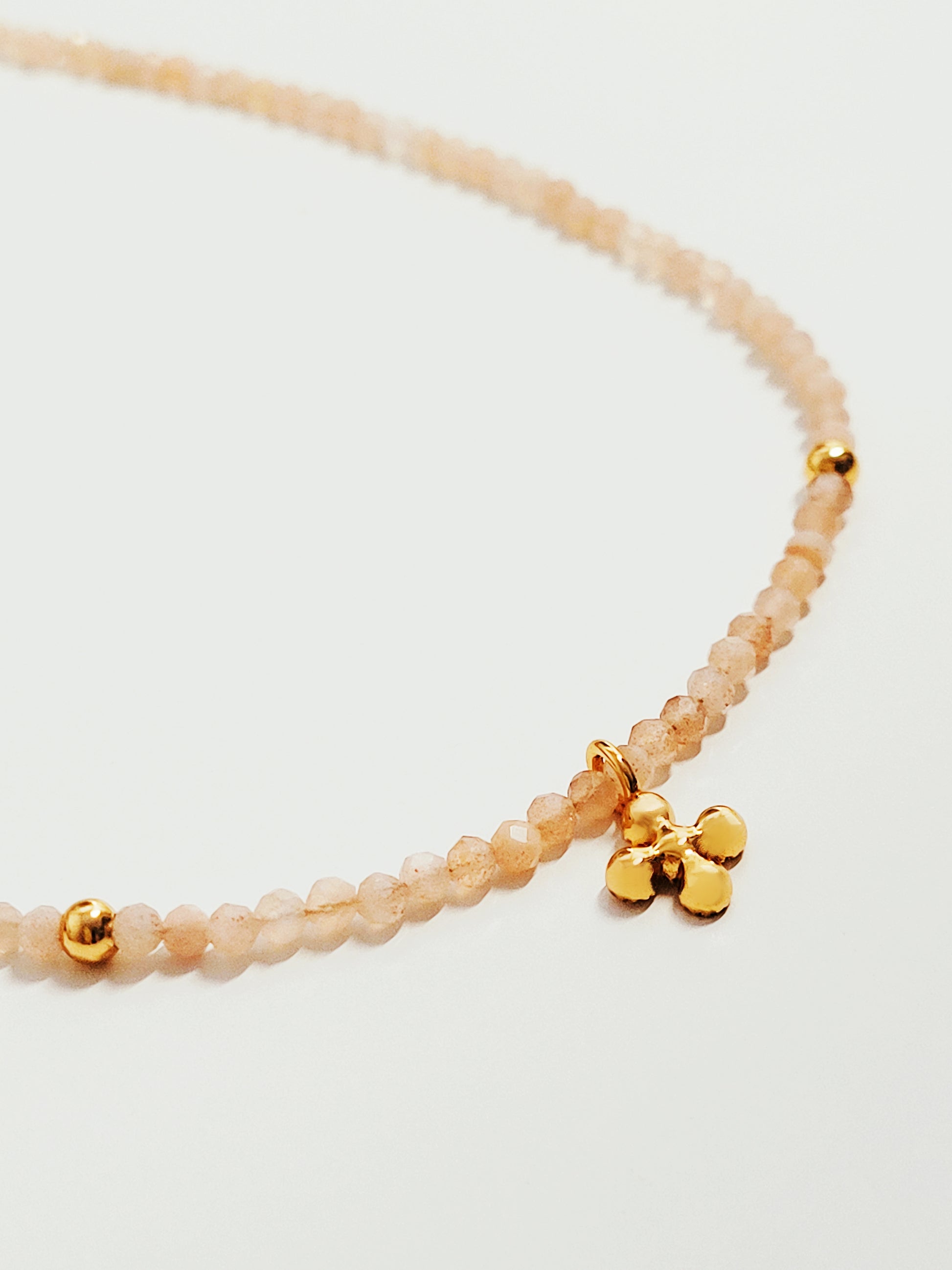 Close-up of a natural sunstone gemstone choker necklace with gold plated beads and a two-sided clover charm. Symbolizing good luck to someone wearing it.