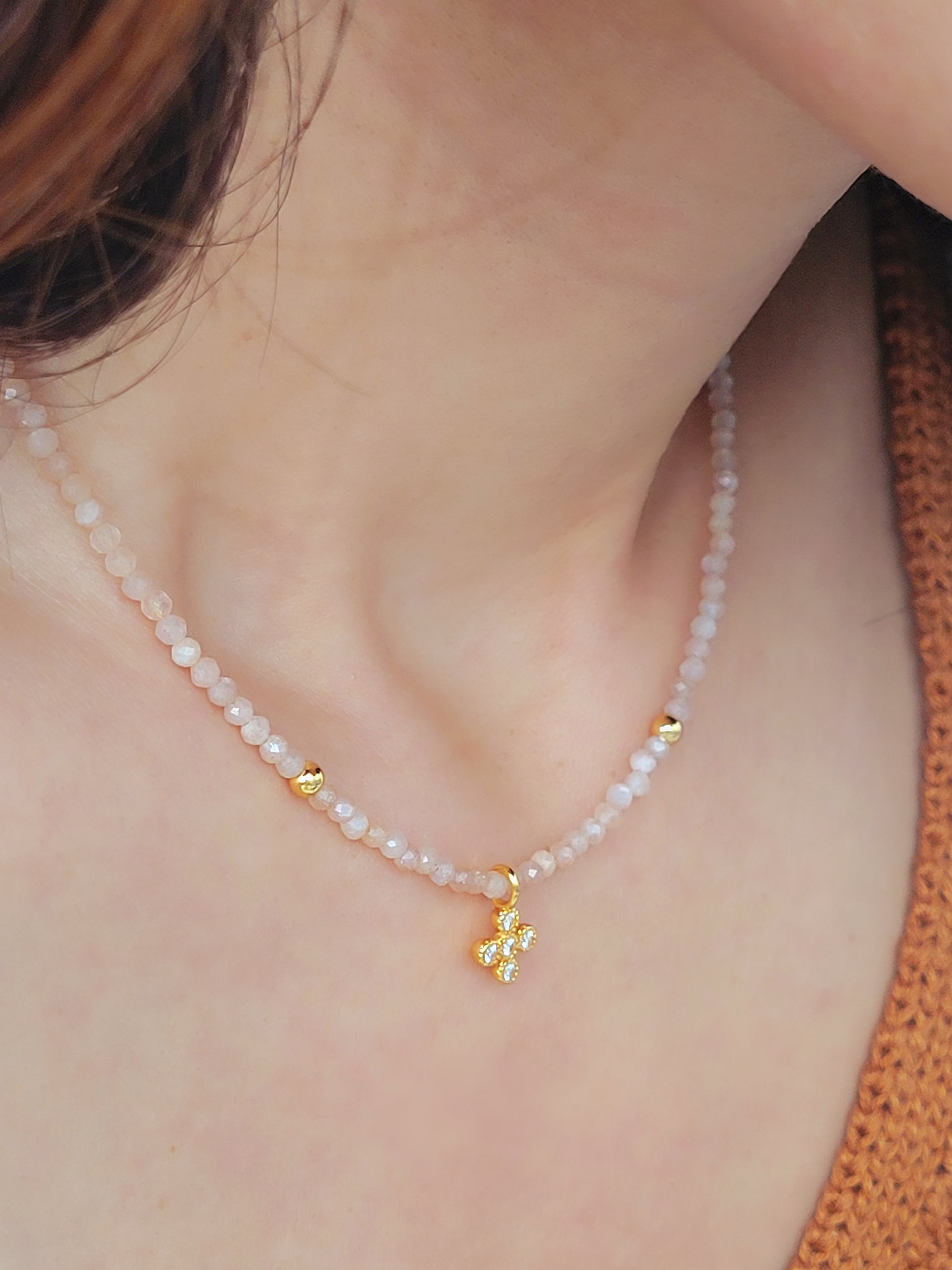 Close-up of a woman wearing an elegant sunstone beaded necklace with a mini clover pendant in gold.