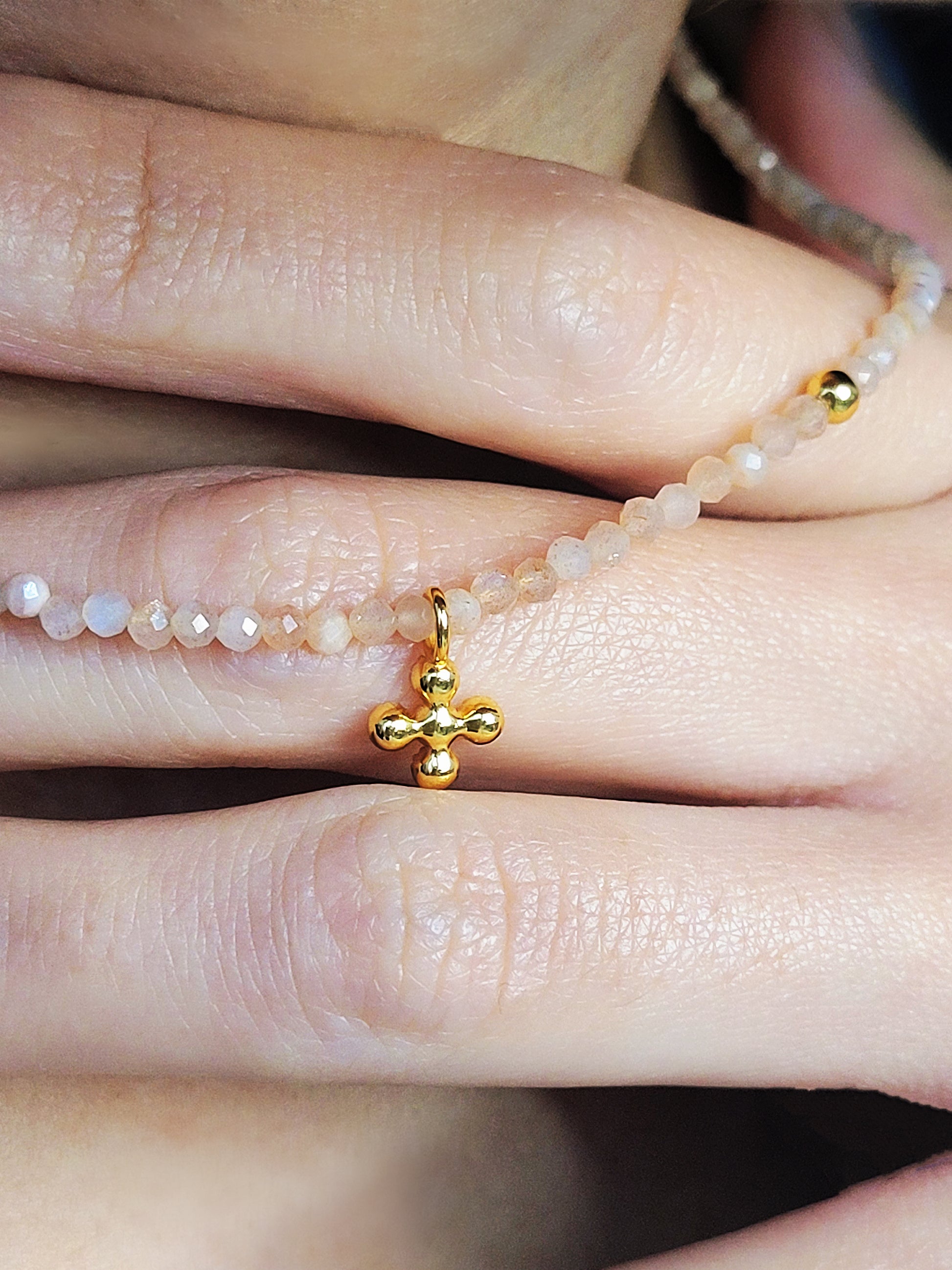 Close-up of a woman’s hand holding a sunstone gemstone choker with a cross pendant.