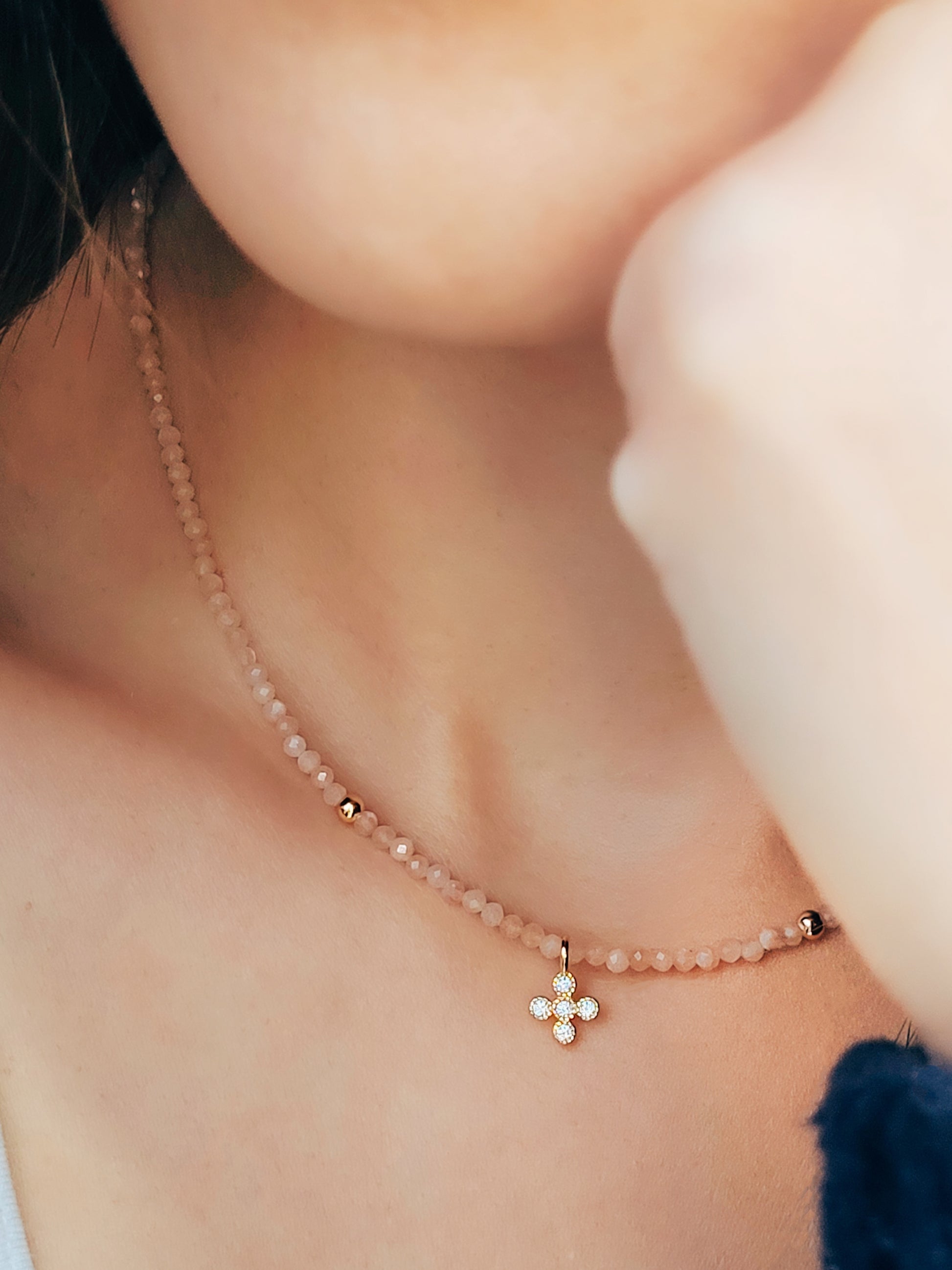 Close-up of a woman wearing an elegant sunstone beaded necklace with a mini clover pendant in gold.