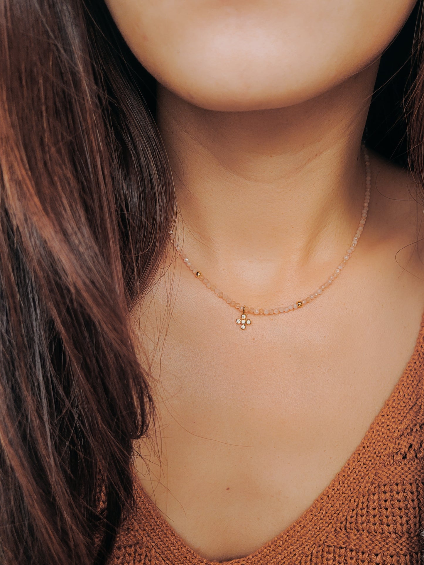 Close-up of a woman wearing an elegant sunstone beaded necklace with a mini clover pendant in gold.