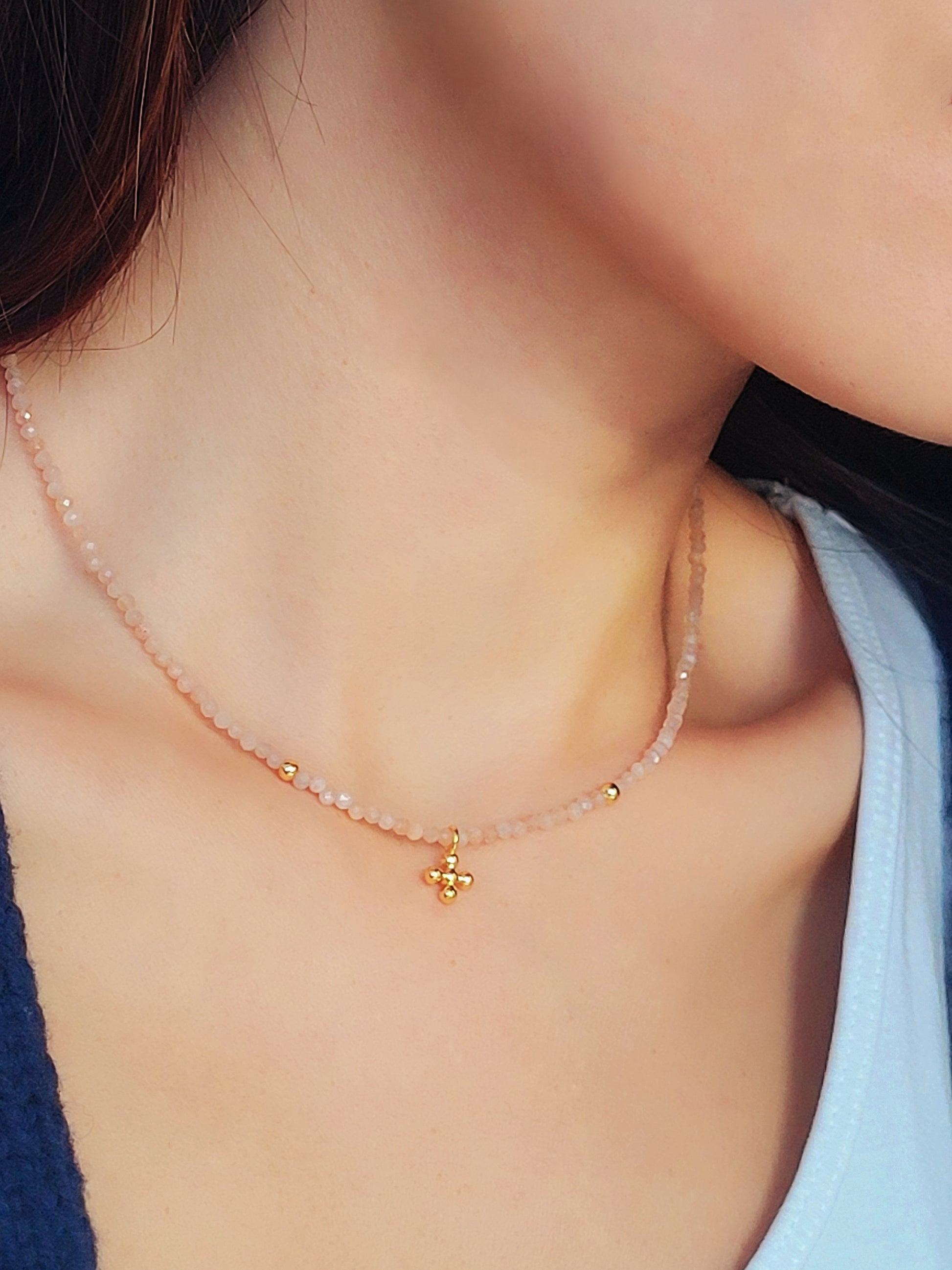 Close-up of a woman wearing an elegant sunstone beaded necklace with a mini clover pendant in gold.