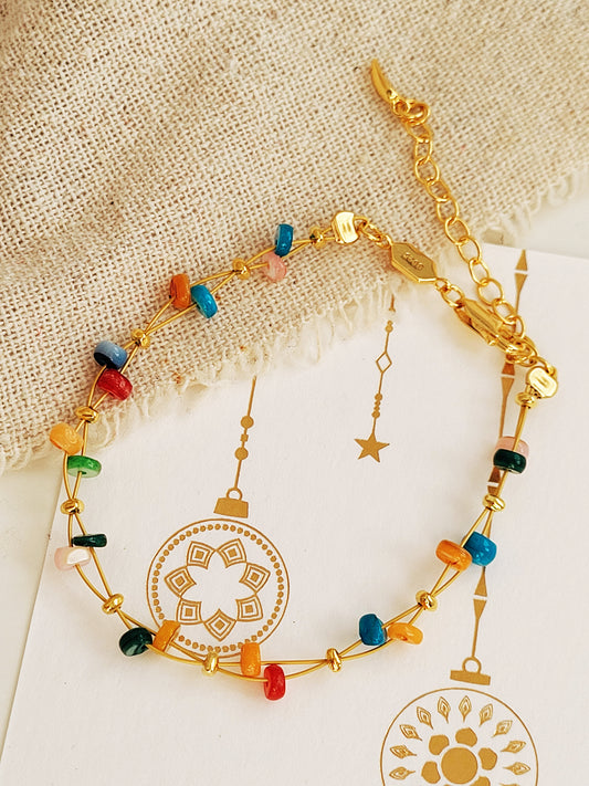 Gold bracelet with colorful onyx gemstone beads on a textured beige surface