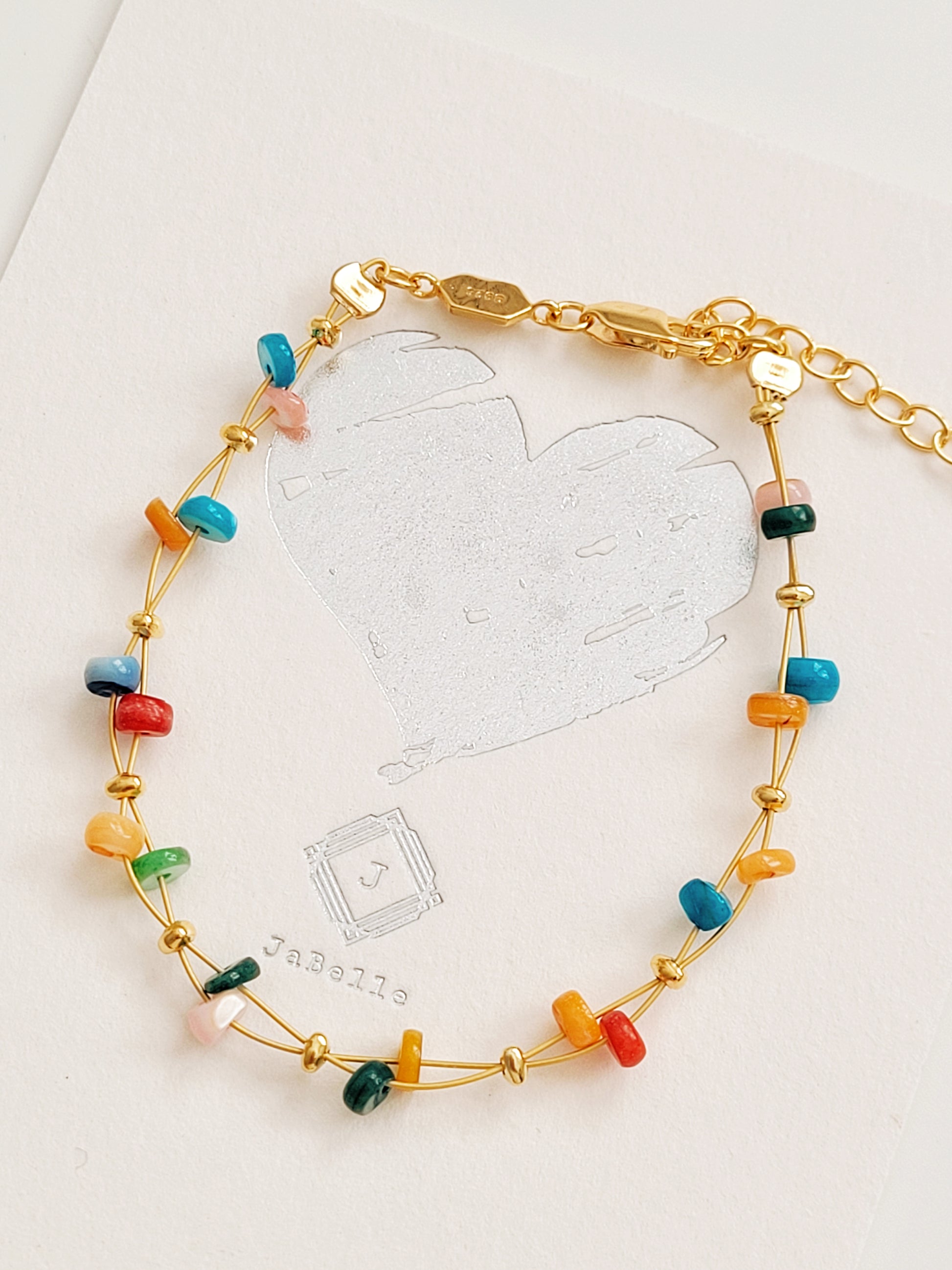A gold beaded bracelet with multi-colored onyx gemstone displayed on a gift message card