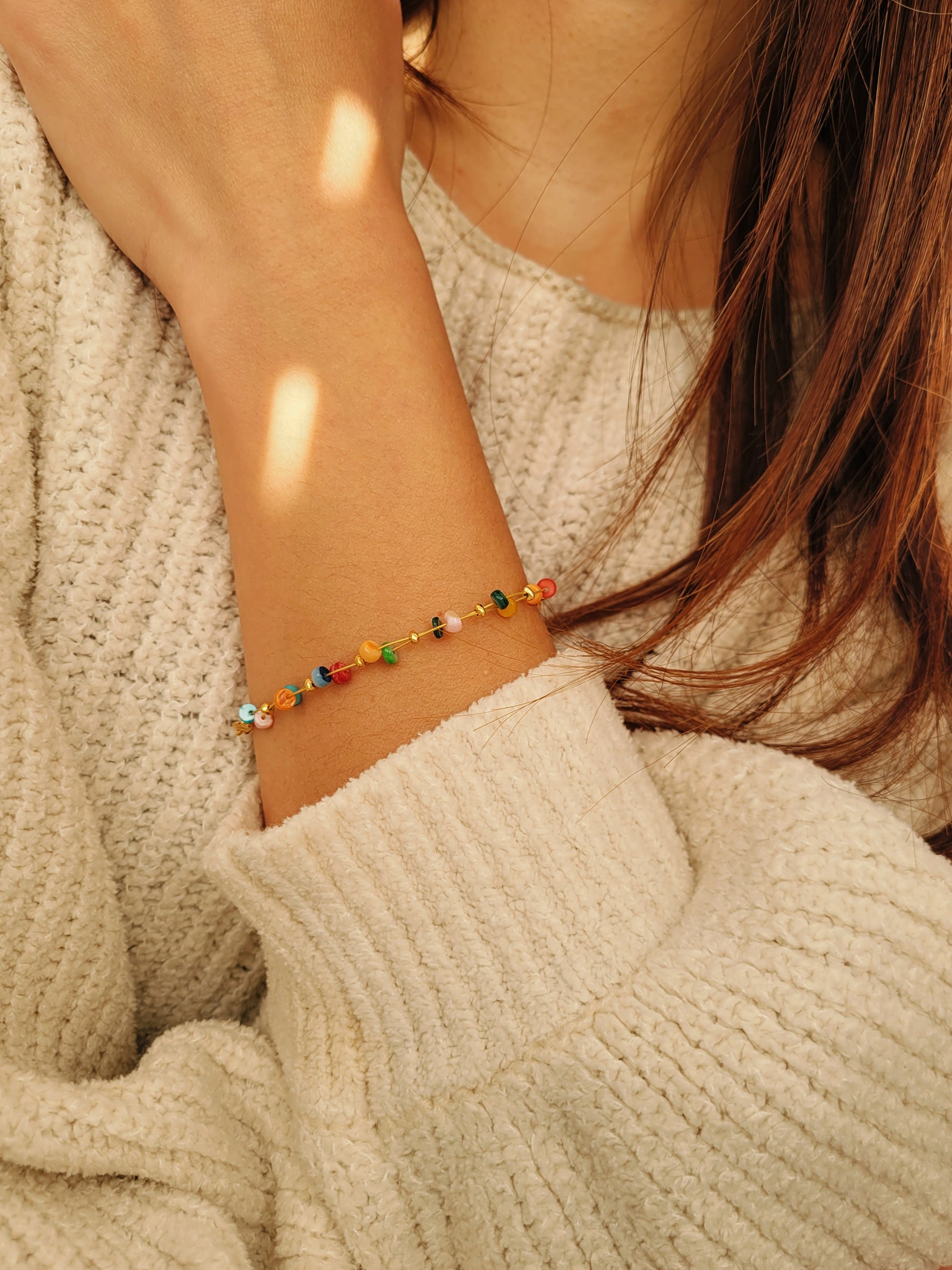 Close-up of a woman wearing a colorful beaded onyx gemstone bracelet on a beige sweater.
