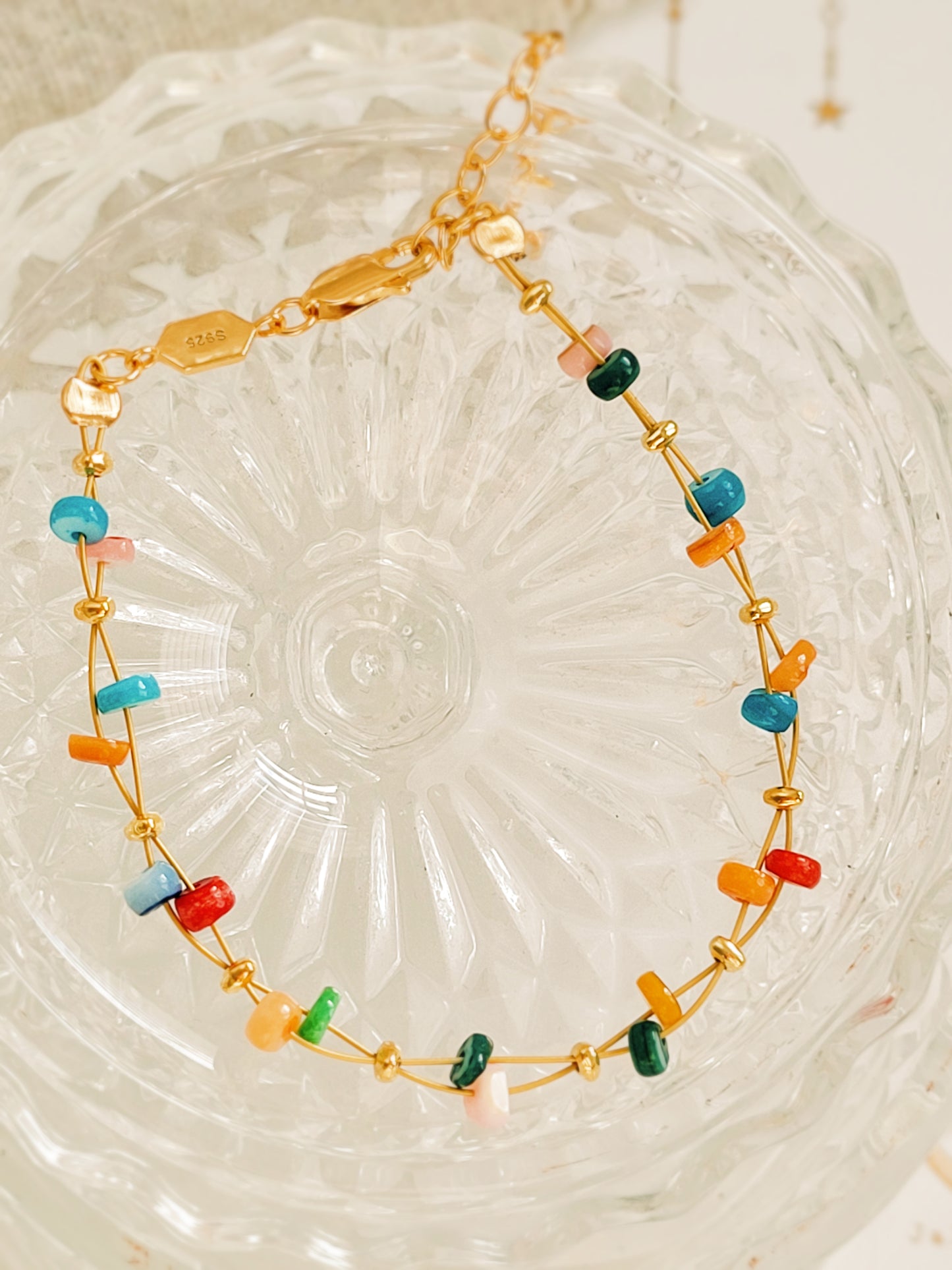 Gold bracelet with colorful beads on a textured glass surface