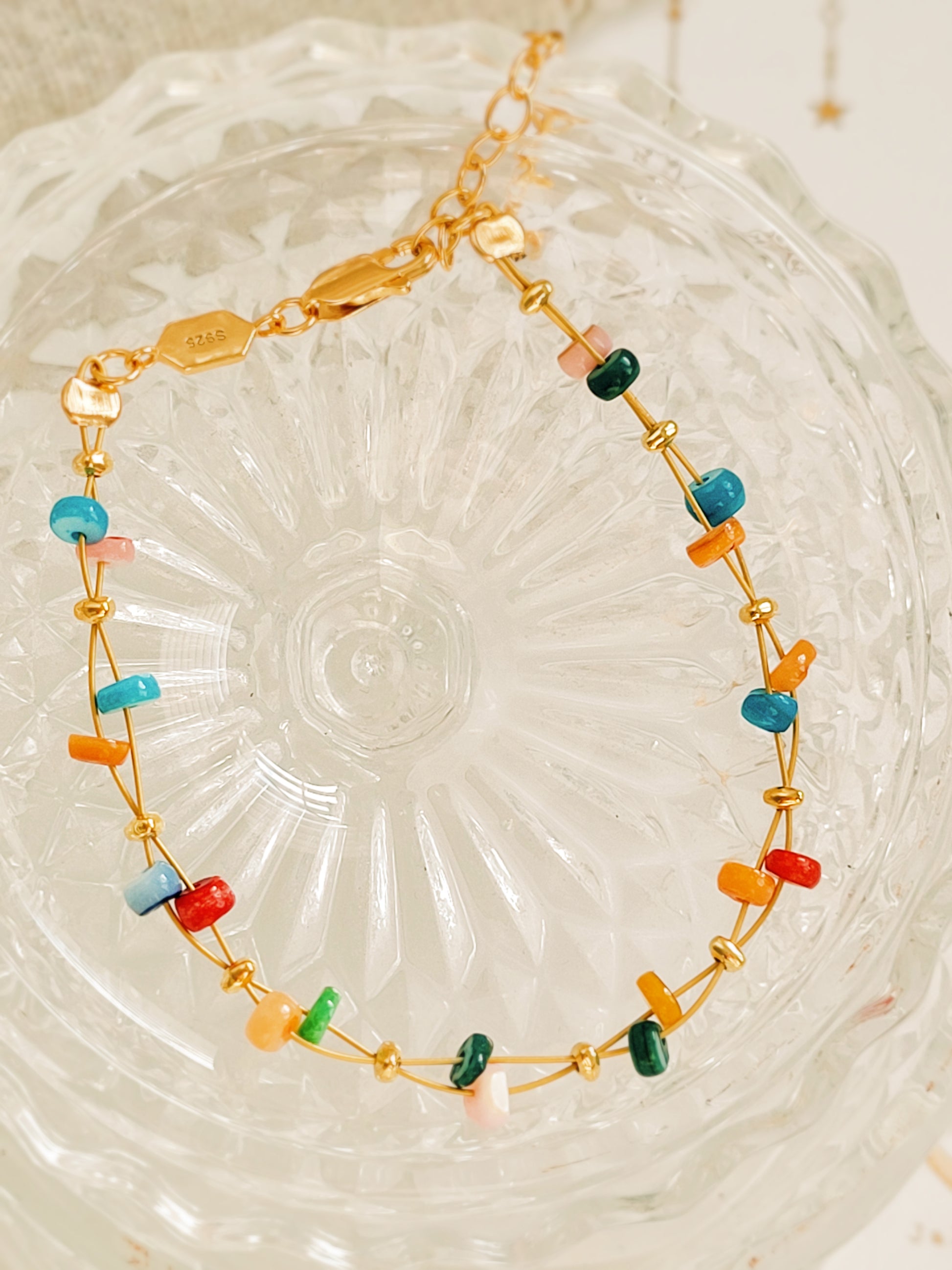 Gold bracelet with colorful beads on a textured glass surface