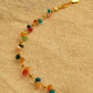 Multicolored beaded bracelet on a gold chain against a beige fabric background